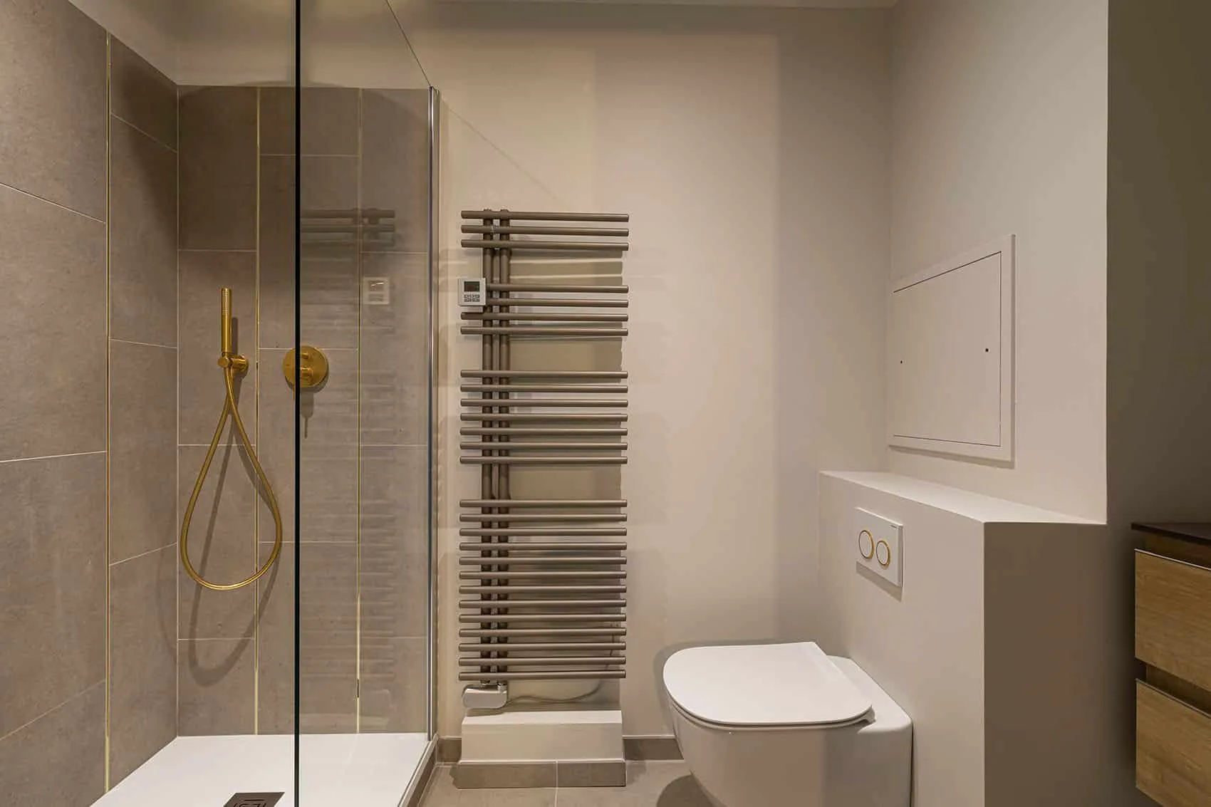 Salle de douche des invités : paroi vitrée, robinetterie dorée, sèche-serviettes et WC suspendu sur faïence beige