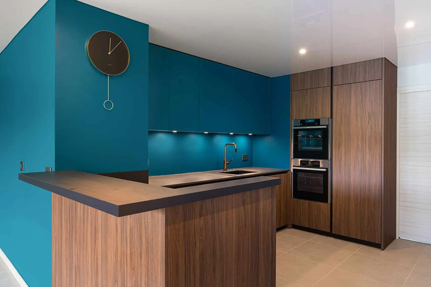 Cuisine ouverte de l’appartement des quais de Saône : façades bleu canard, bois foncé et colonne de fours encastrés