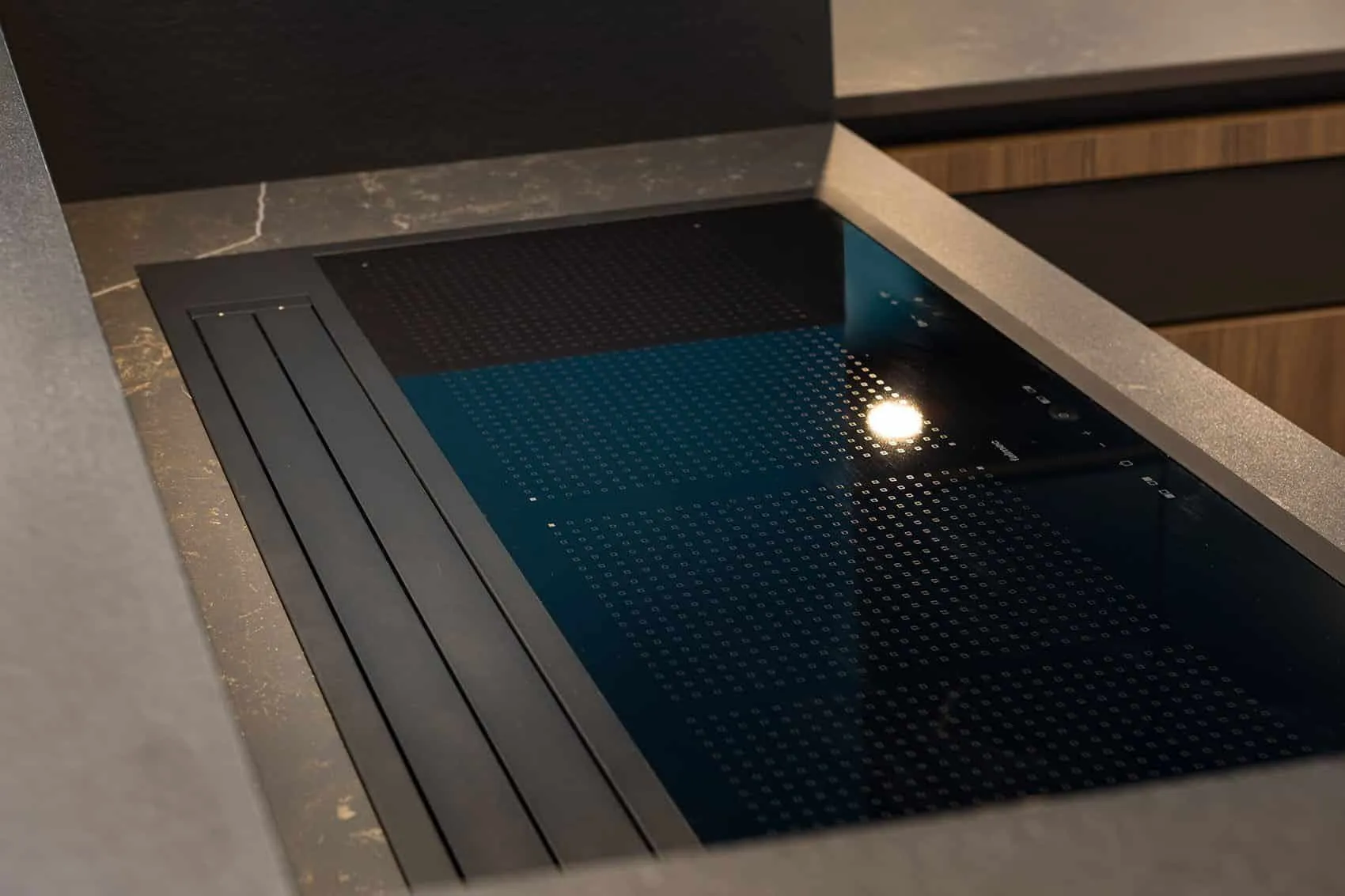 Table de cuisson noire encastrée et sa grille d’aspiration intégrée dans le plan de travail gris de la cuisine