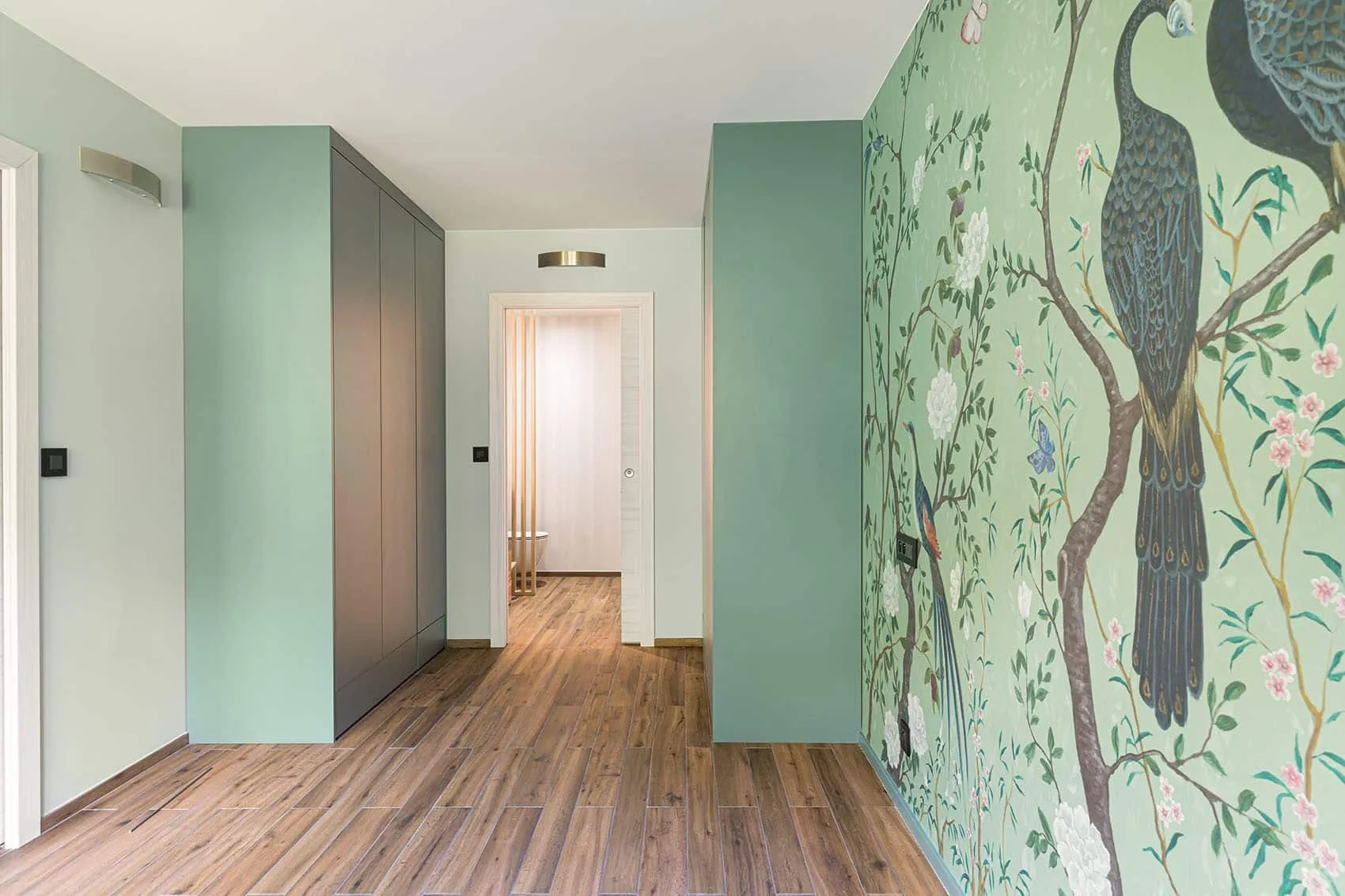 Rénovation d’appartement à Lyon : couloir aux placards gris et vert d’eau face au panoramique végétal au paon