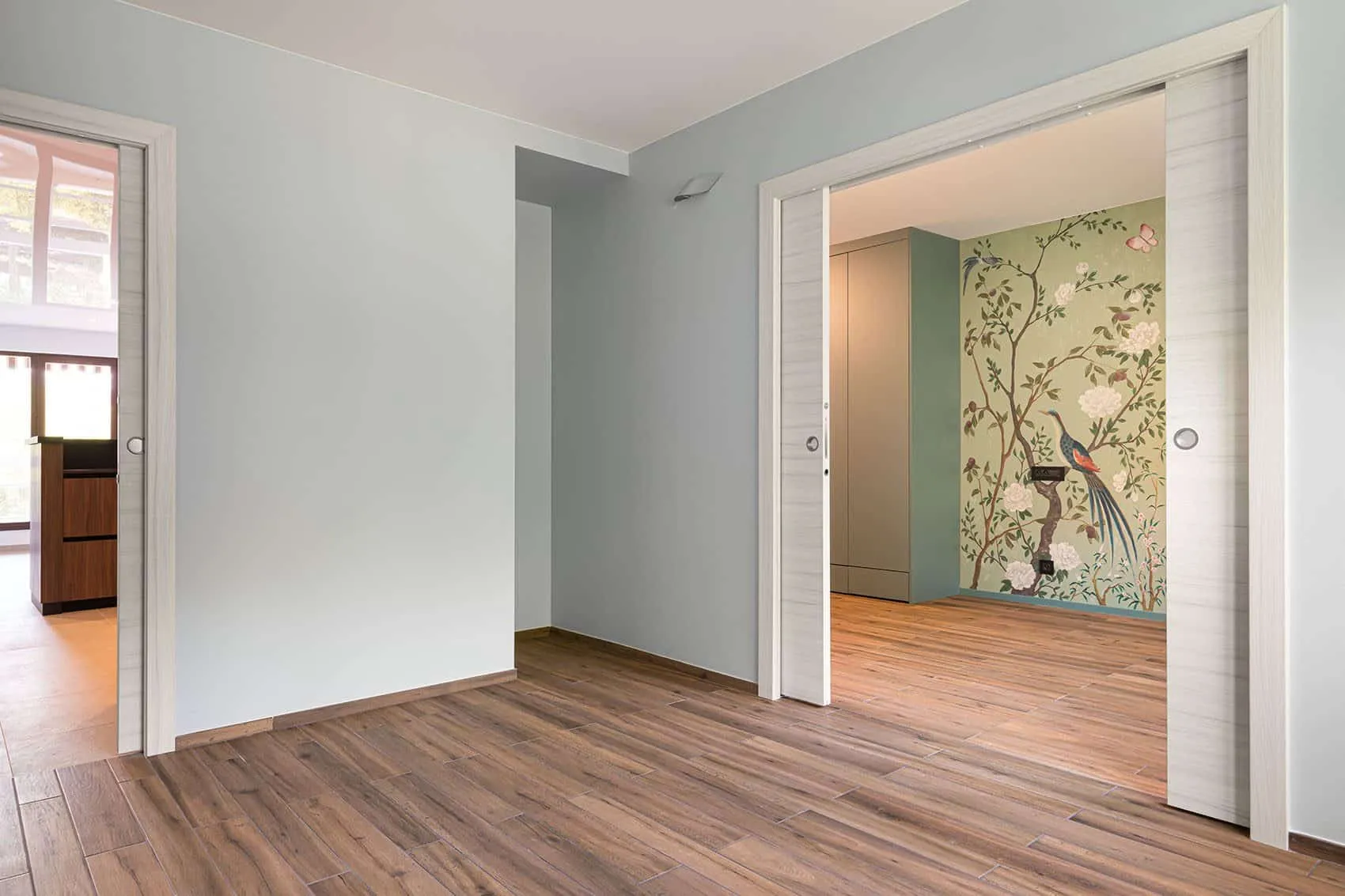 Chambre ouverte par des portes coulissantes à galandage sur la pièce au papier peint à paon, sol bois