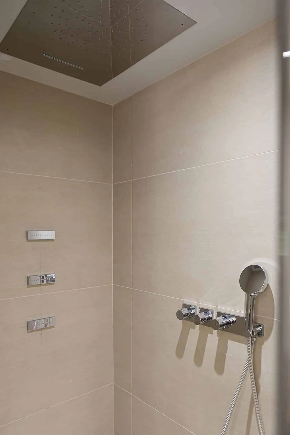 Paroi de douche en grand carrelage beige avec robinetterie encastrée et douchette, salle d’eau de la suite parentale