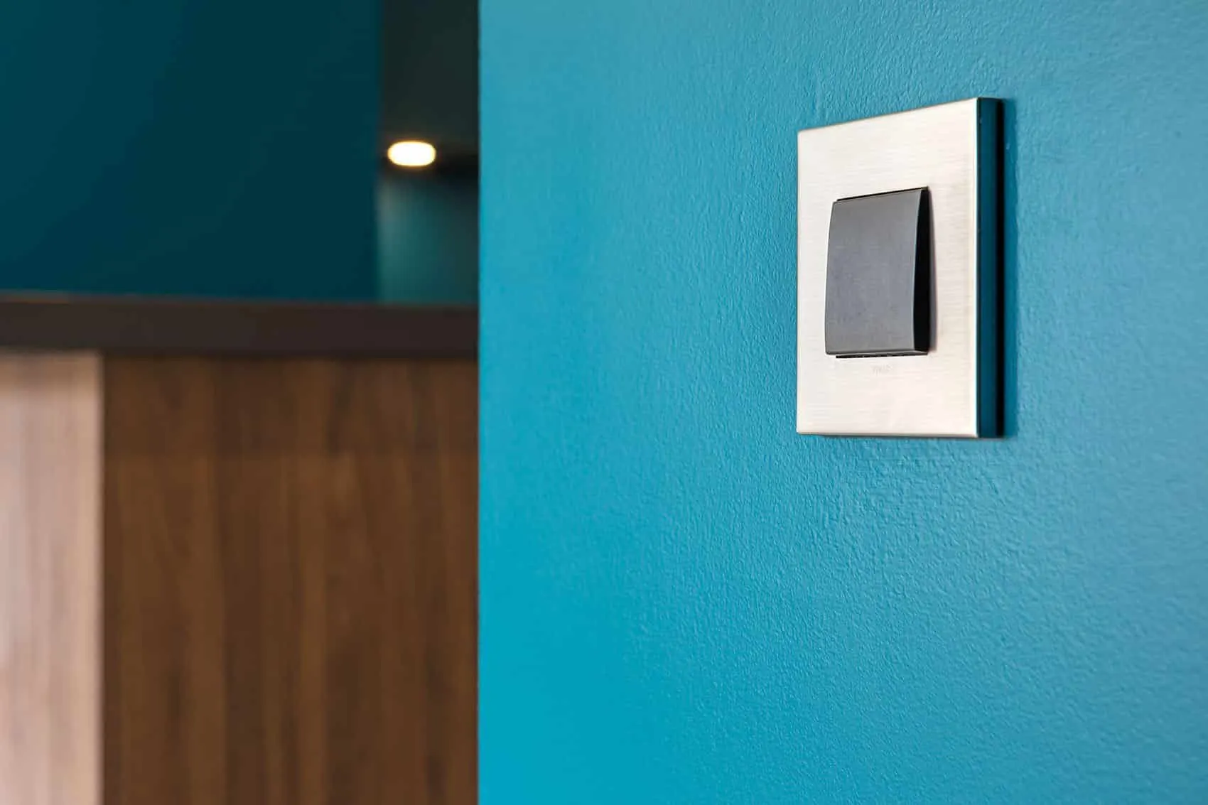 Interrupteur à plaque métal sur un mur bleu canard près de la cuisine, finition soignée par un architecte d’intérieur à Lyon