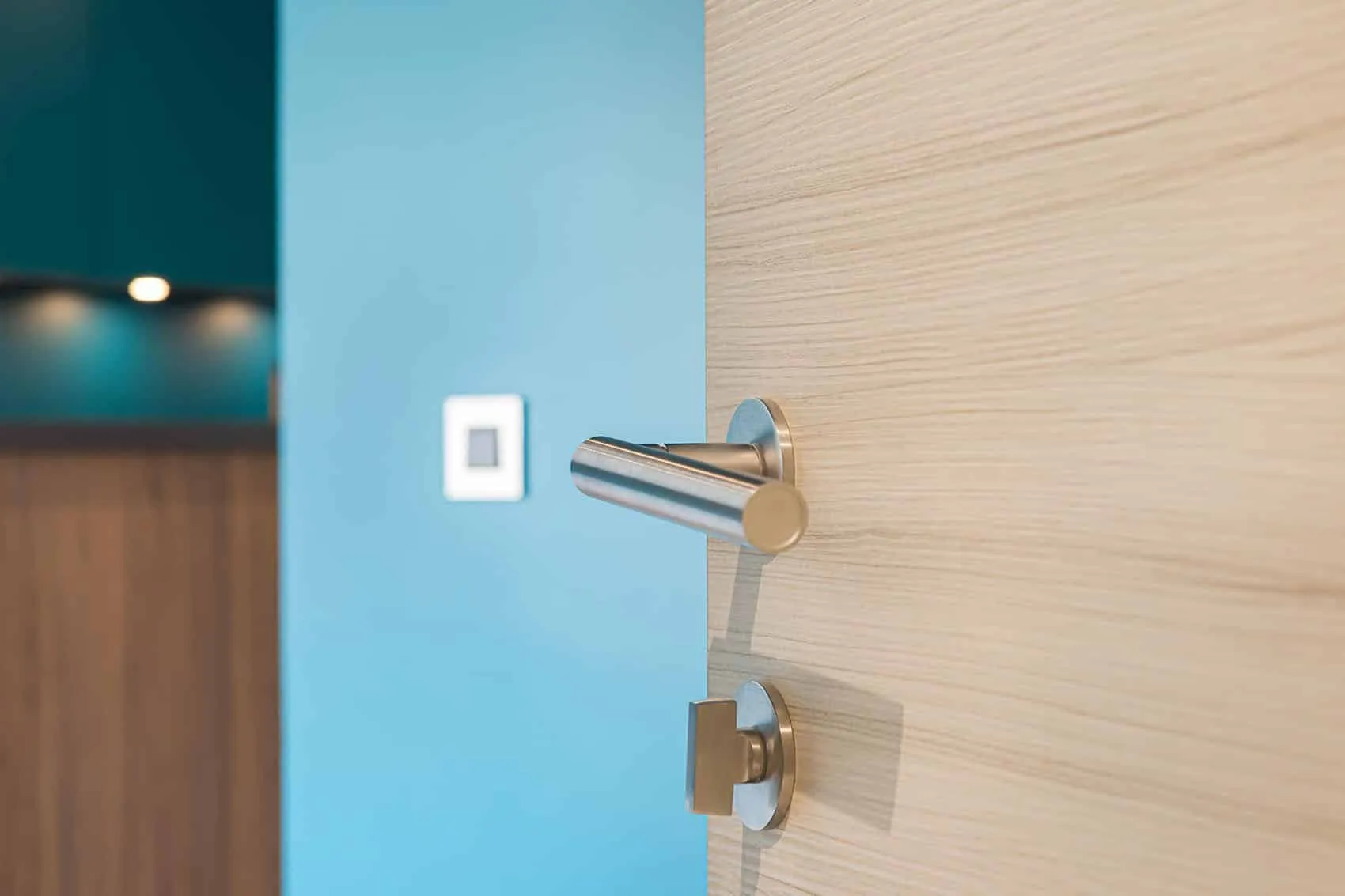 Poignée de porte en métal sur une porte effet bois clair, mur bleu canard et cuisine en arrière-plan