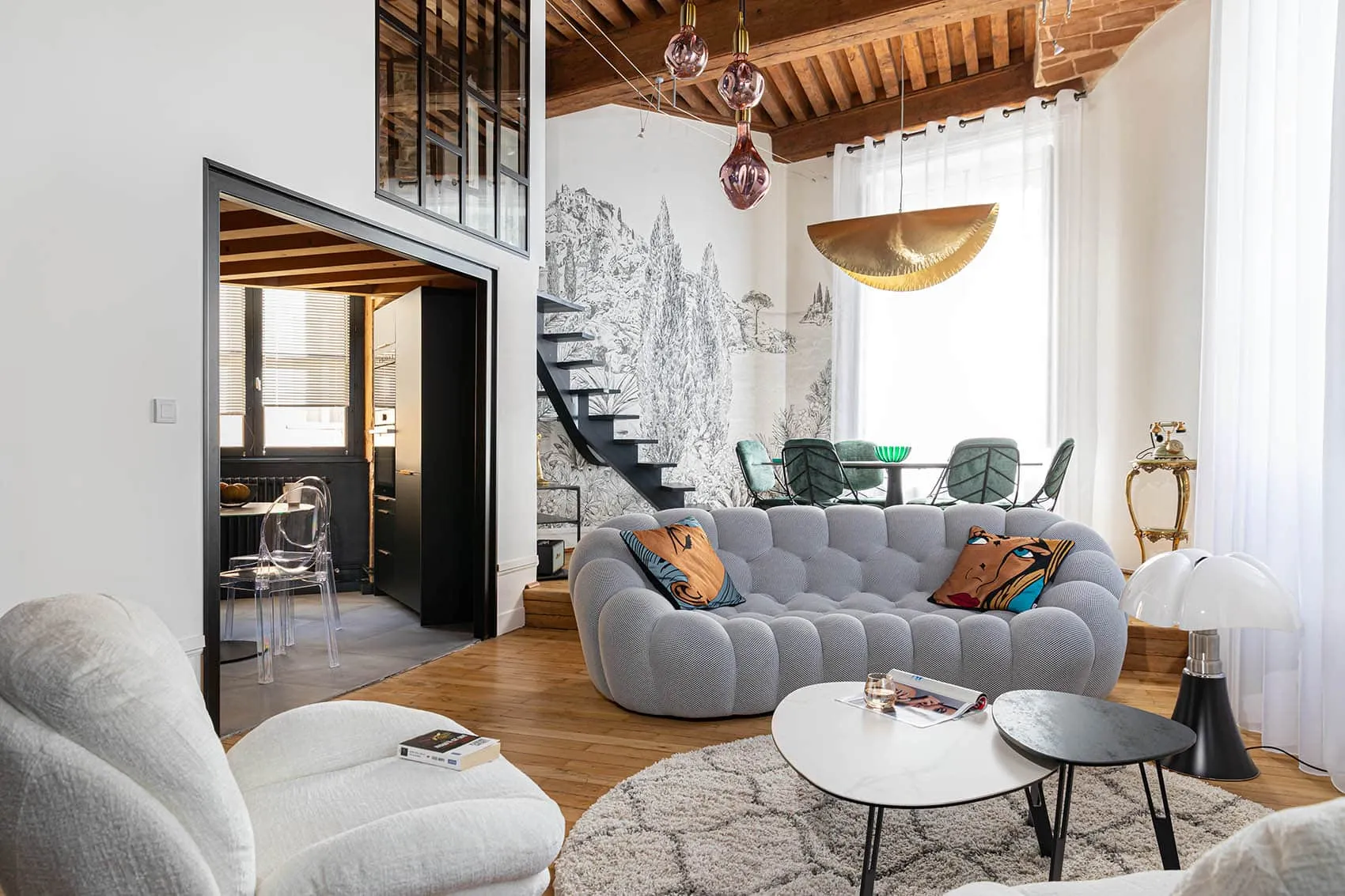 Salon d’un appartement de canut relooké à Lyon : canapé gris arrondi, papier peint panoramique, plafond à la française et verrière