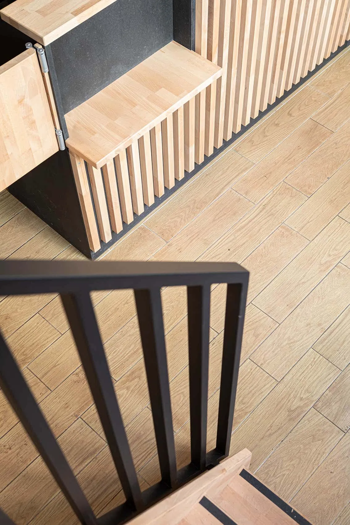 Détail de l’escalier : garde-corps en métal noir à barreaux et marches en bois clair, style industriel du restaurant