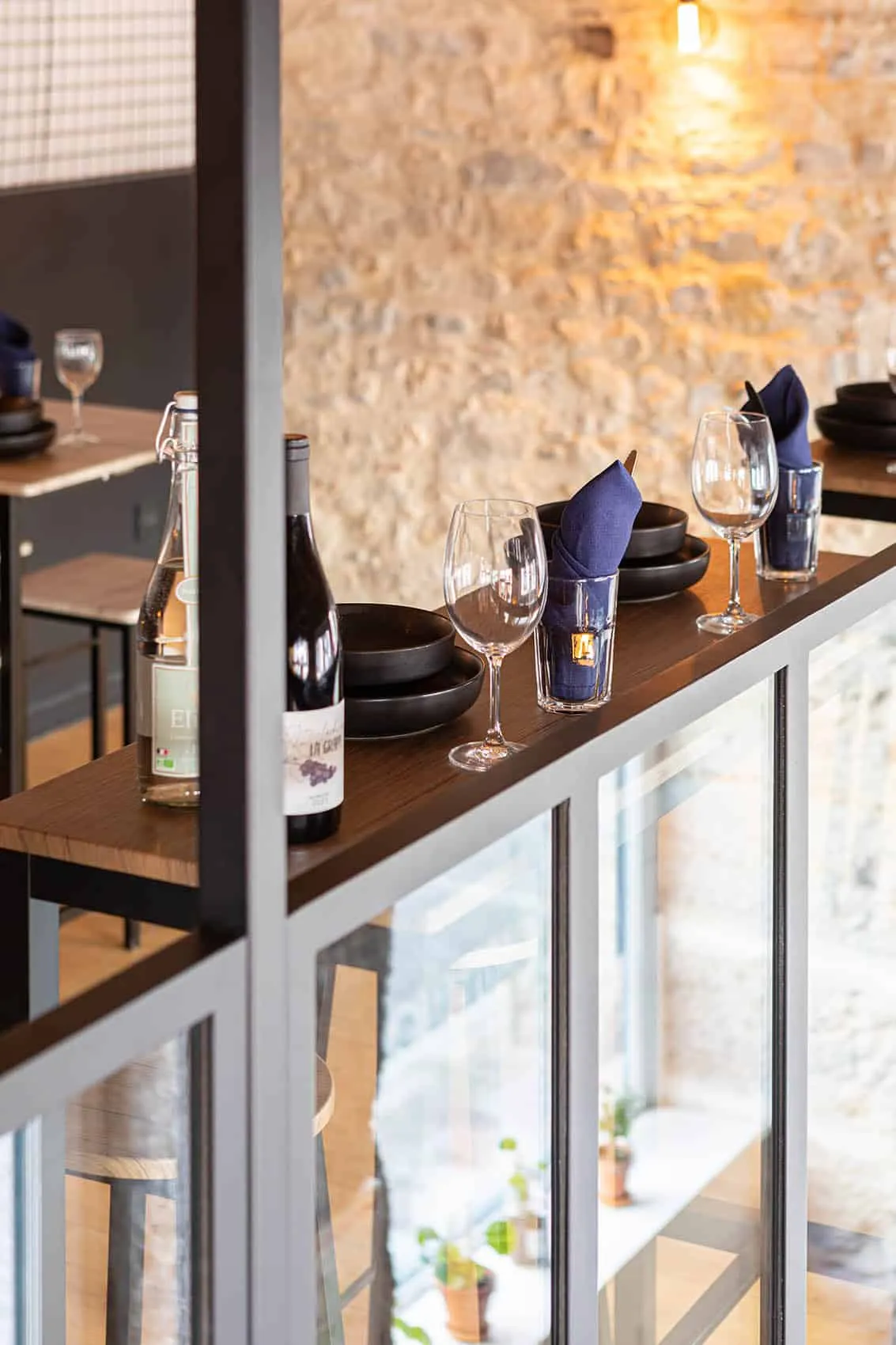 Tablette en bois dressée avec vins, verres à pied, bols noirs et serviettes bleues le long du garde-corps métallique