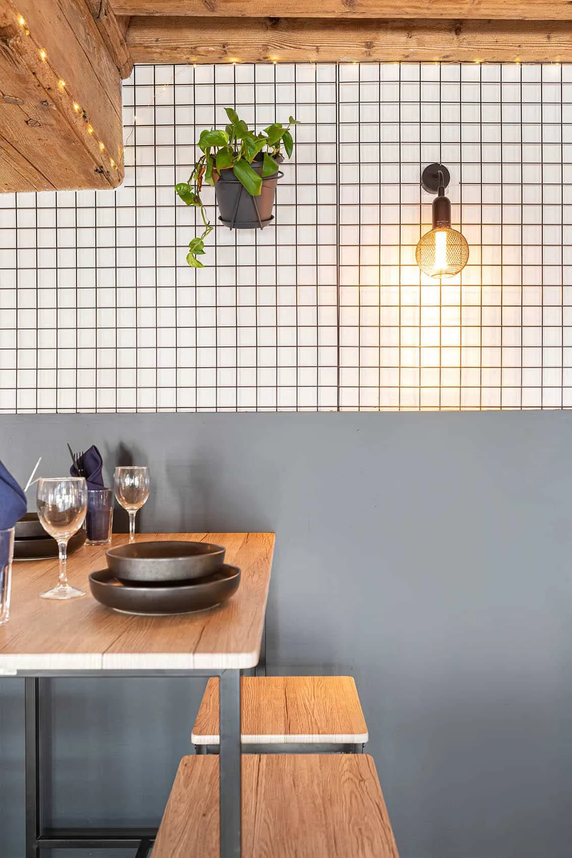 Table dressée devant un mur en carrelage blanc à joints noirs et soubassement gris anthracite, aménagement de restaurant