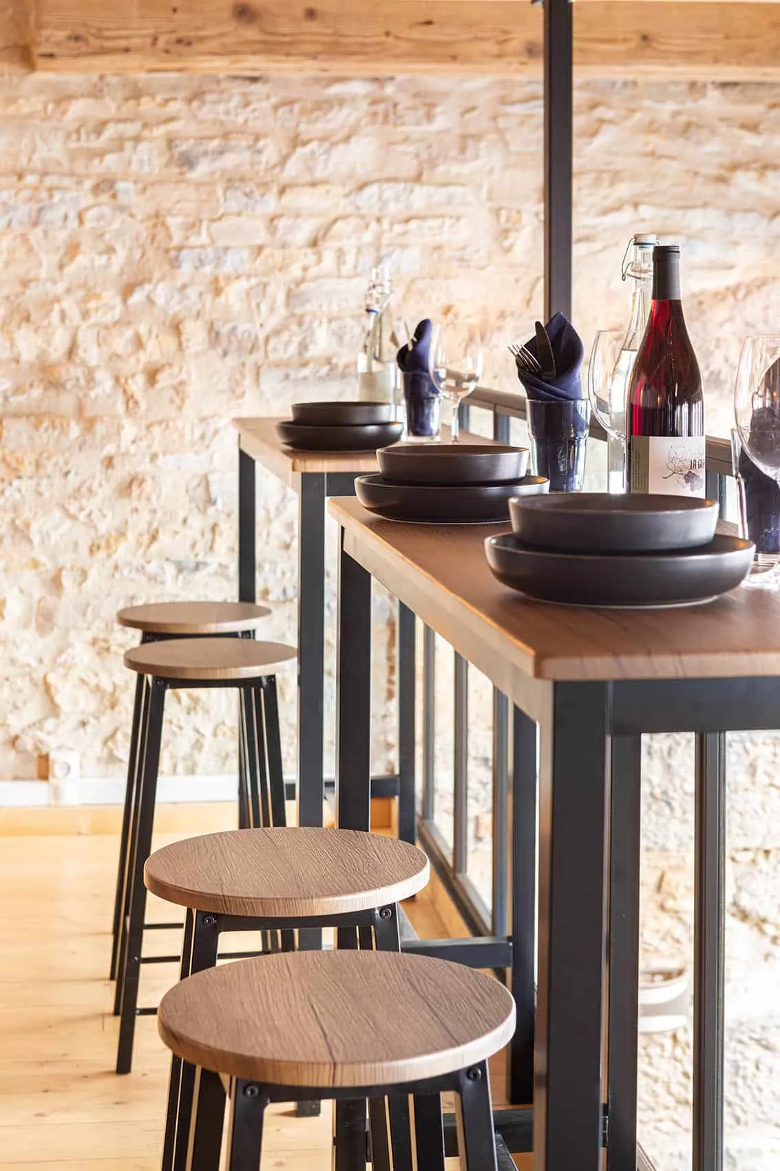 Mange-debout contre le mur en pierre du Dérobé, bols noirs empilés, bouteilles de vin et tabourets en bois