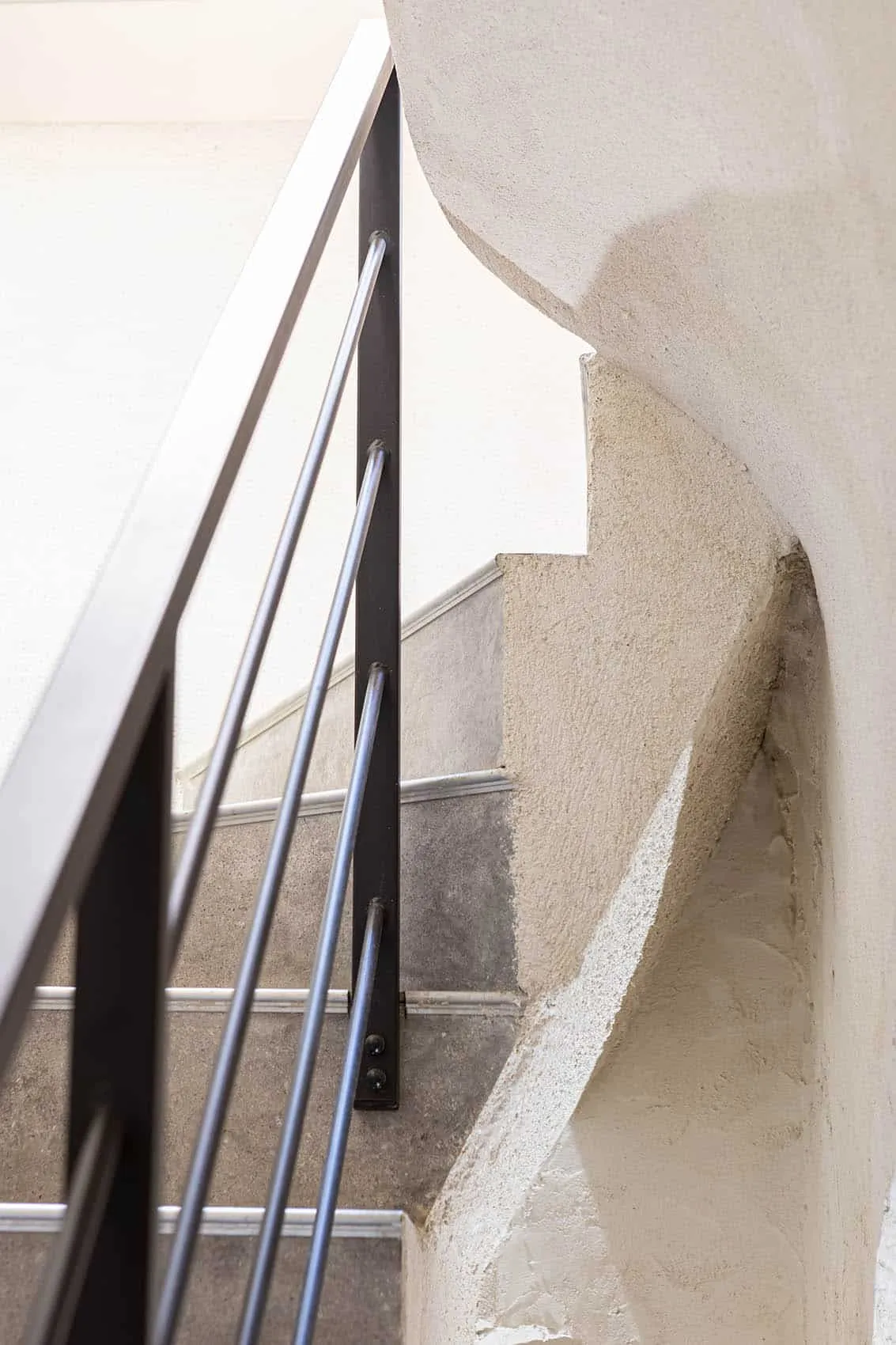 Escalier vers la cave voûtée avec rampe en métal noir et murs enduits en courbe, aménagement de restaurant à Lyon