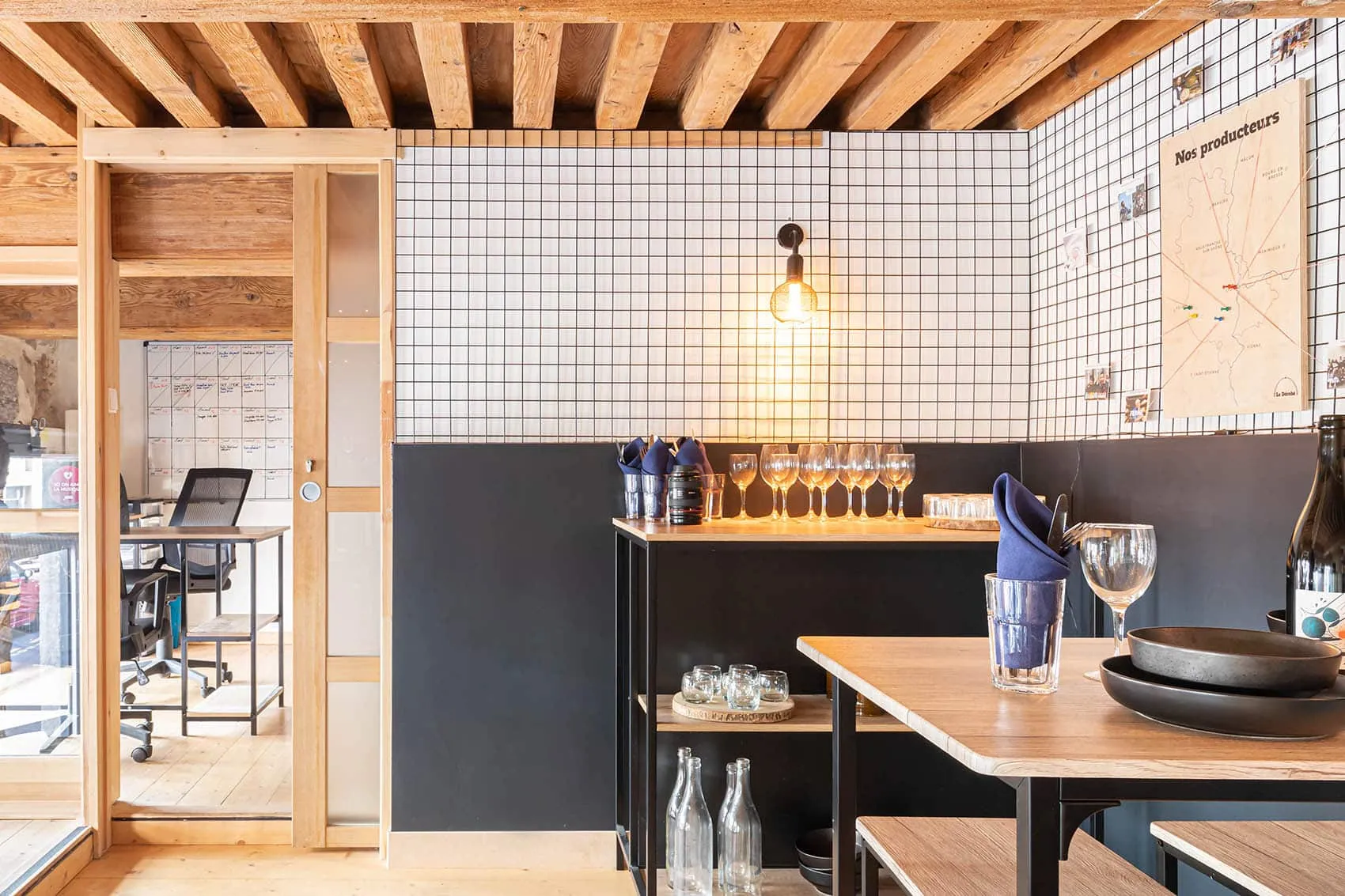 Tables hautes dressées devant un mur en carrelage blanc à joints noirs et soubassement gris, aménagement de restaurant à Lyon