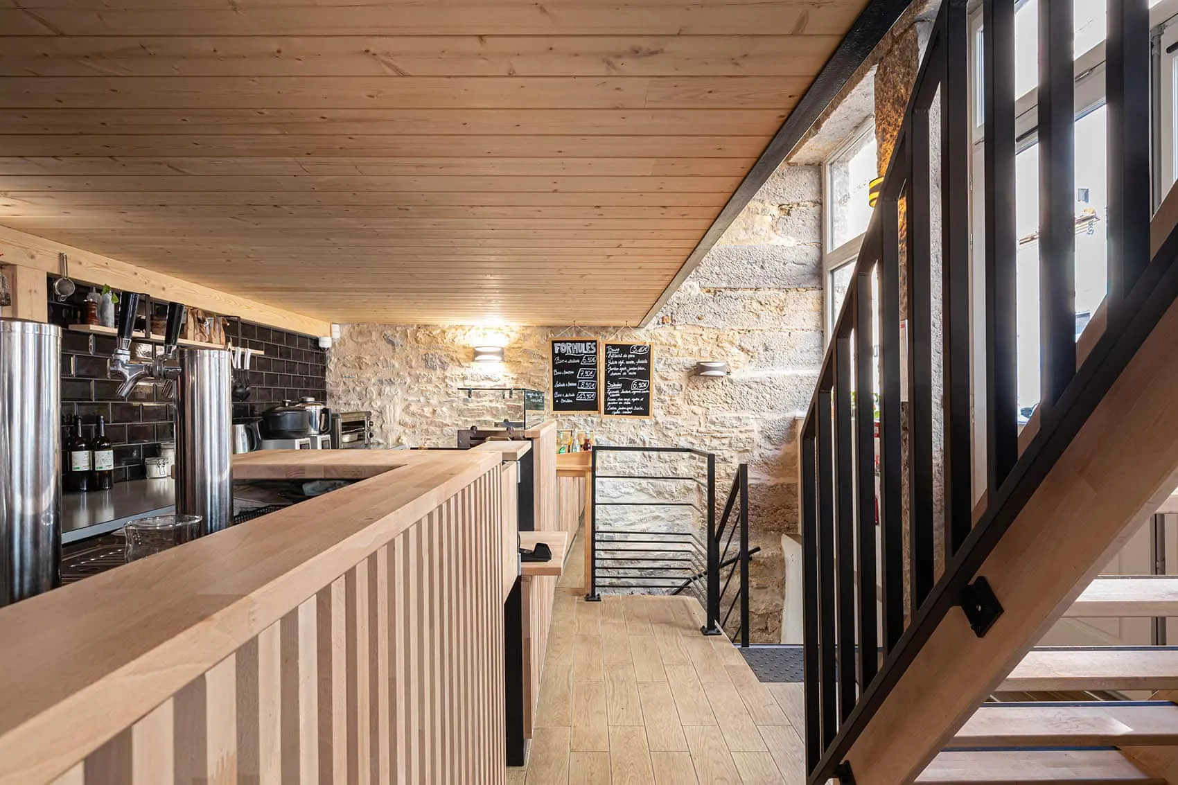 Vue depuis l’escalier en métal noir : comptoir en bois, mur en pierre éclairé et ardoises au mur, Le Dérobé à Lyon