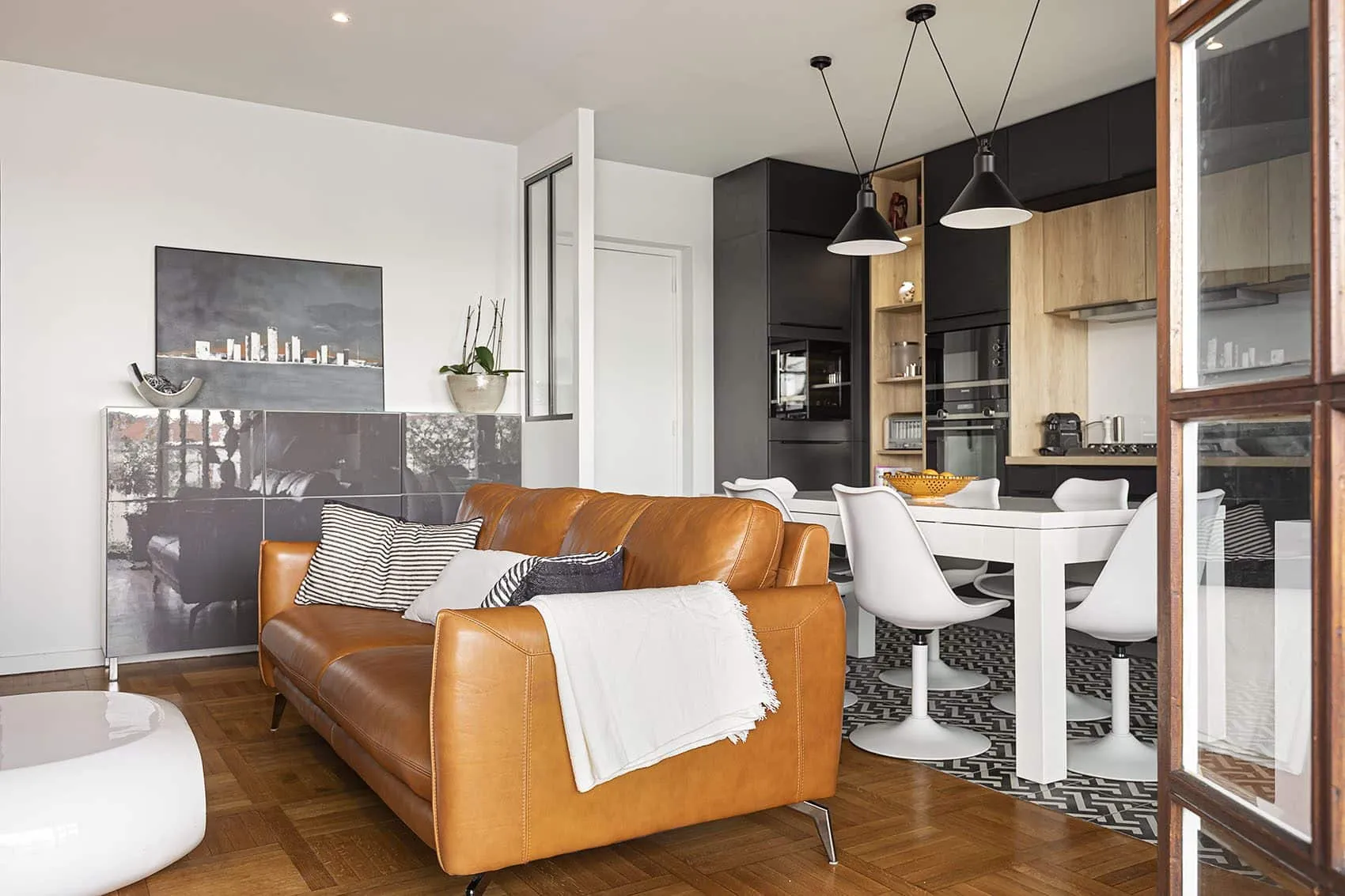 Pièce de vie d’un appartement entièrement rénové rue Deleuvre à Lyon, canapé en cuir et cuisine ouverte