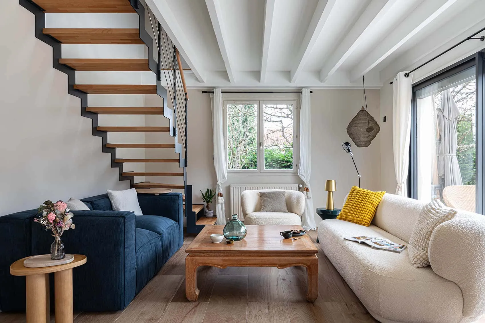 Salon avec canapé bleu, canapé bouclette blanc et table basse en bois au pied de l'escalier, décoration intérieure d'une maison rénovée