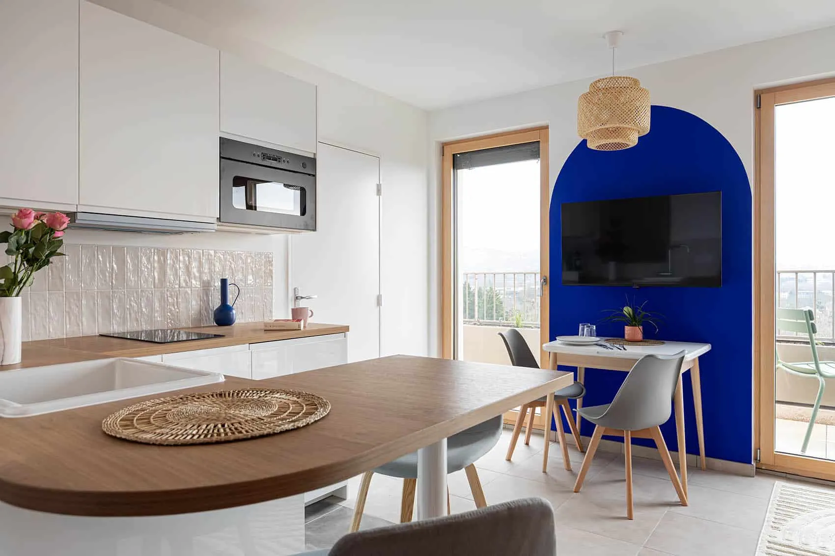 Cuisine blanche et table en bois devant le mur bleu Klein en arche