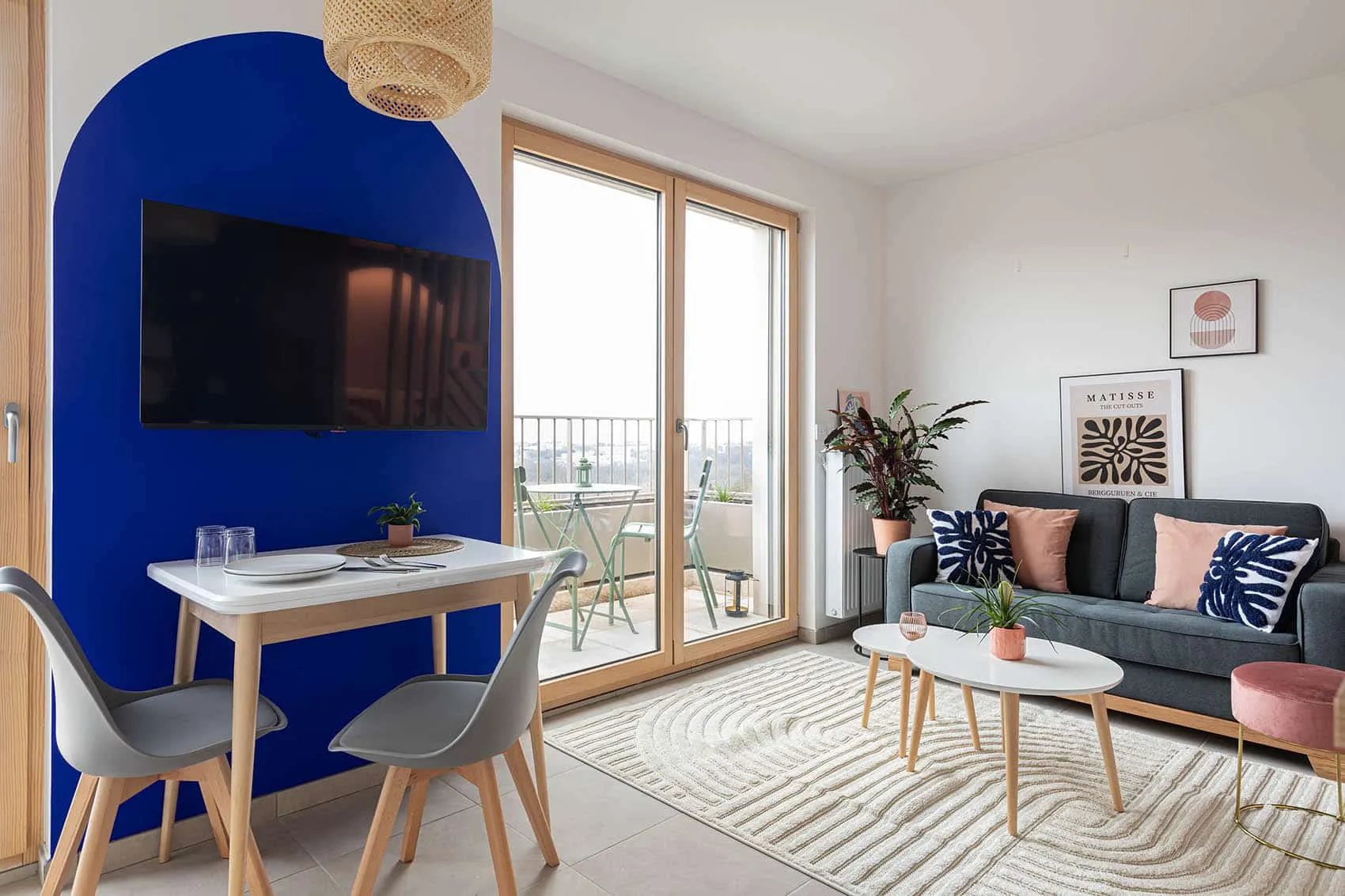 Mur bleu Klein en arche avec télévision, table pour quatre et salon d’un studio neuf personnalisé