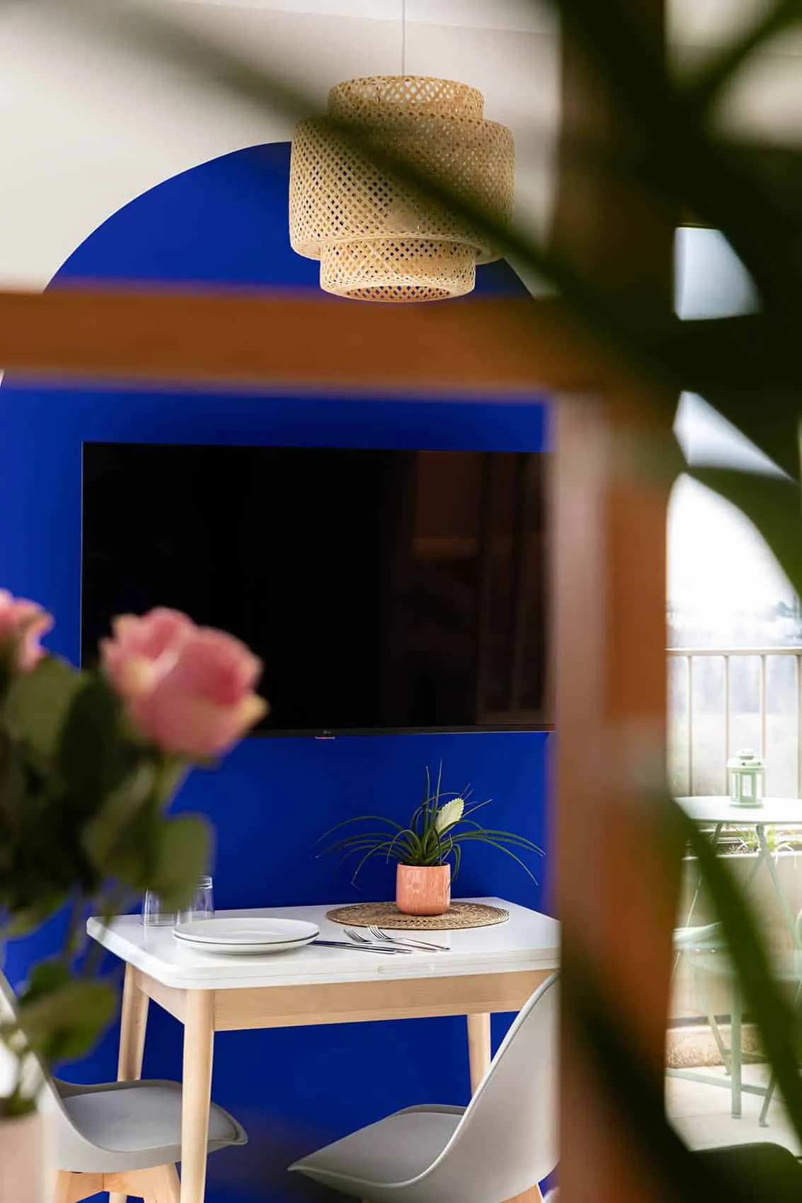 Arche bleu Klein et écran vus à travers les plantes, roses roses au premier plan, ambiance colorée du studio