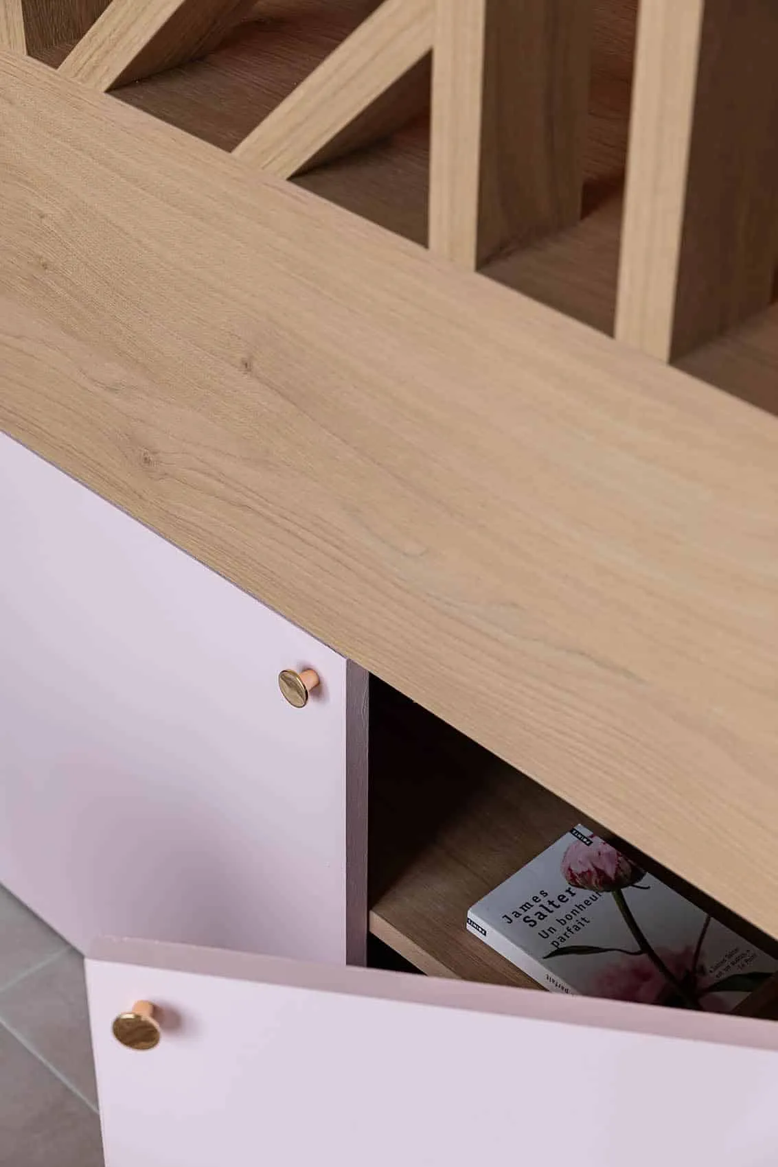 Coffre de rangement rose aux boutons dorés sous un banc en bois clair, claustra ajourée au-dessus