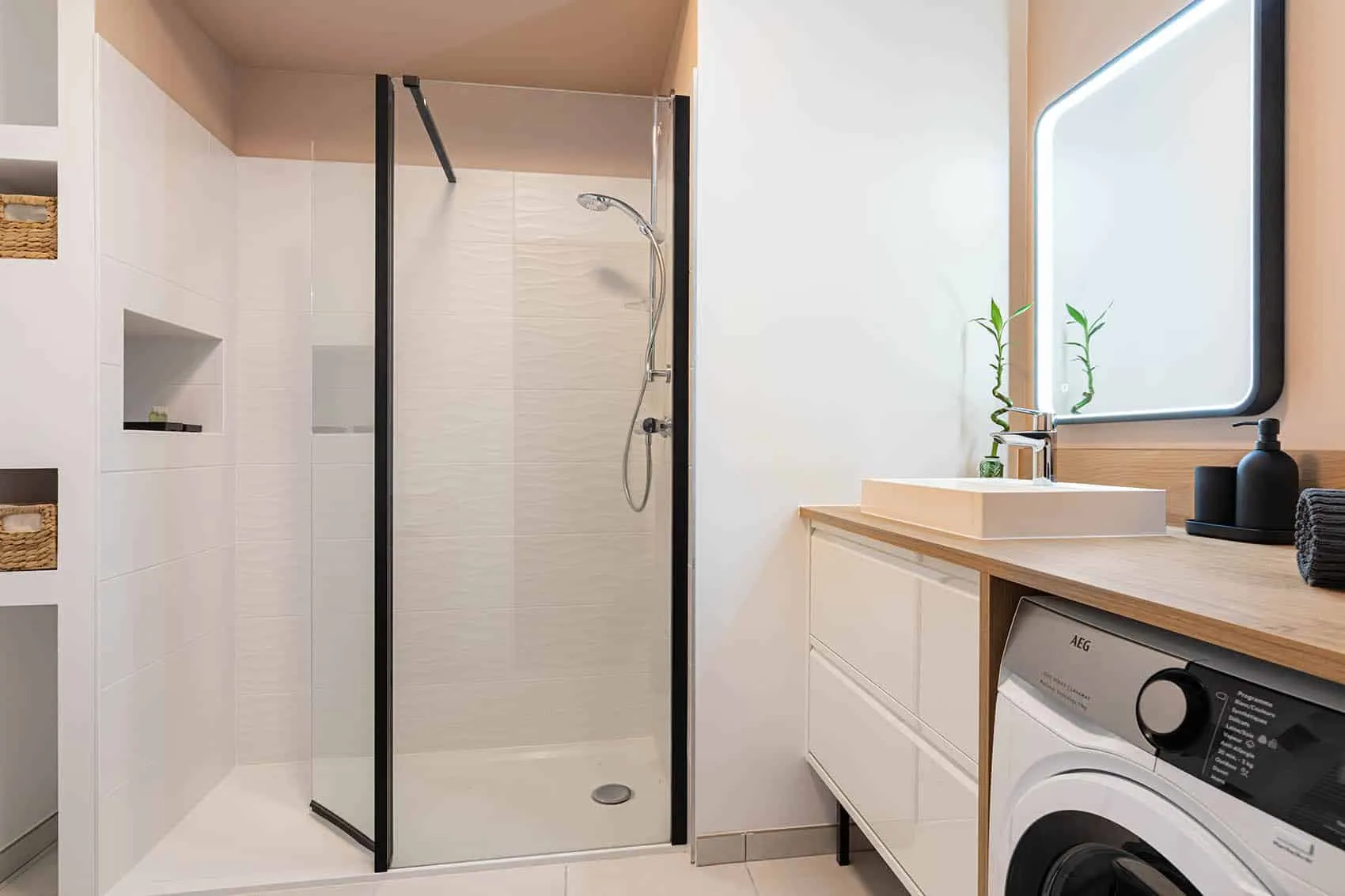Salle d’eau d’un studio neuf : douche à paroi vitrée, niches, vasque posée et lave-linge intégré