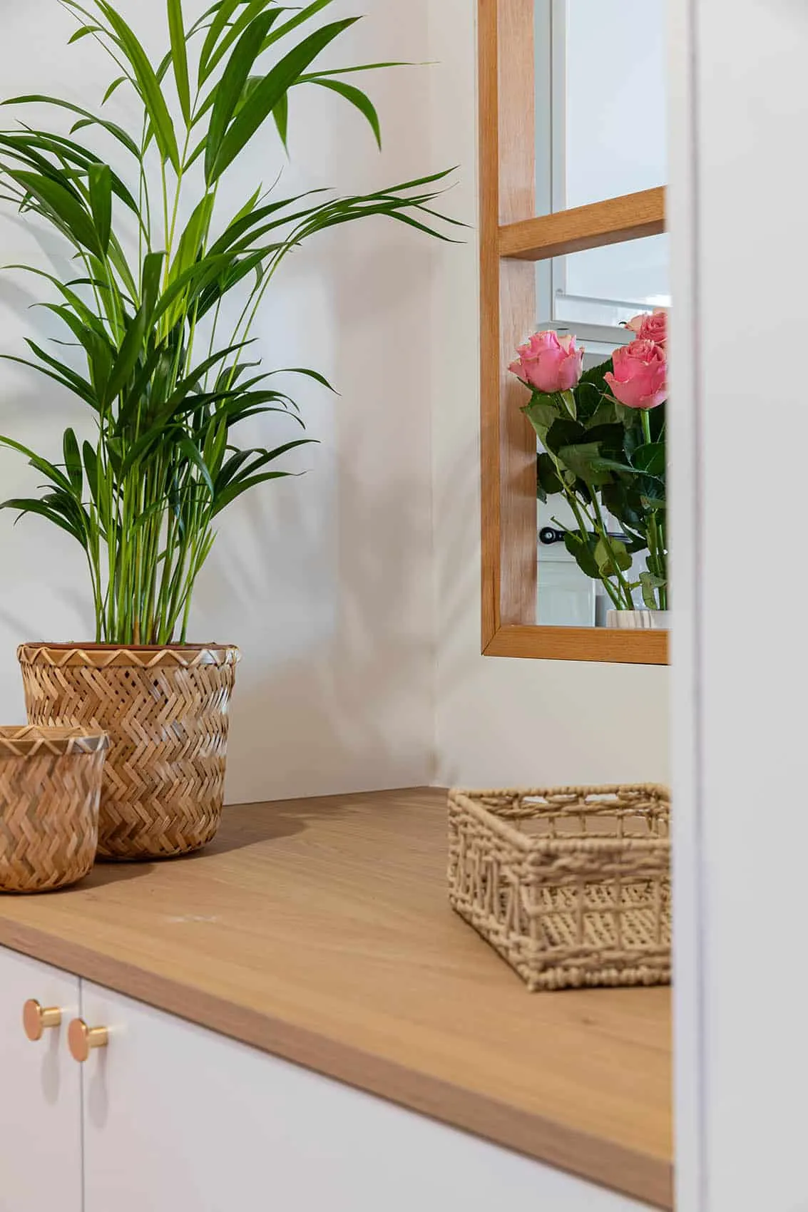 Entrée du studio VEFA : plante en pot tressé sur meuble blanc, fenêtre intérieure en bois et bouquet de roses