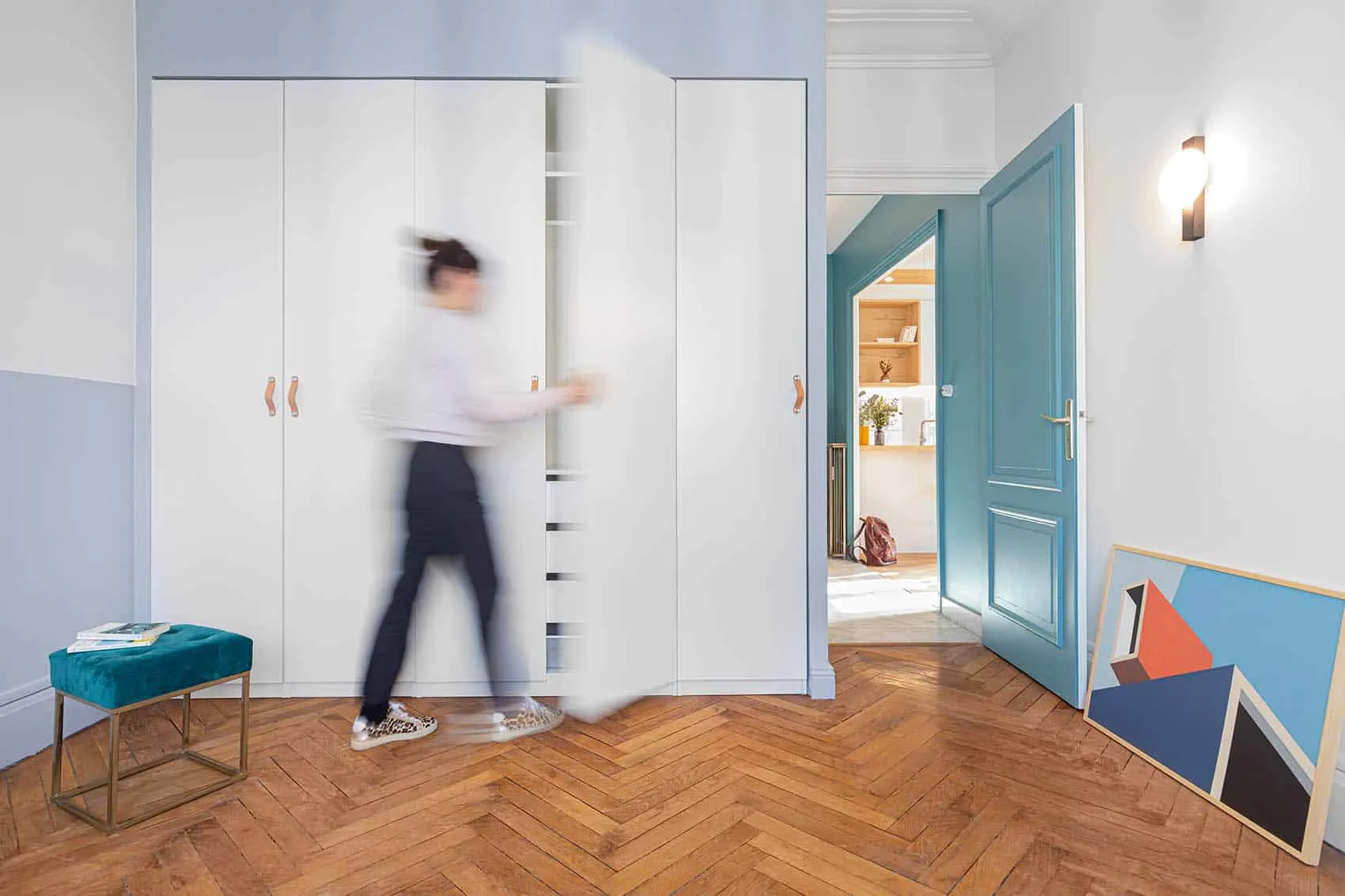 Chambre au parquet à chevrons : dressing blanc toute hauteur, pouf bleu canard et porte moulurée bleue