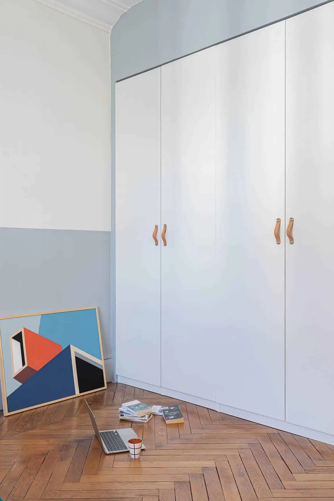 Dressing sur mesure blanc à poignées en cuir, soubassement bleu-gris et tableau graphique posé au sol