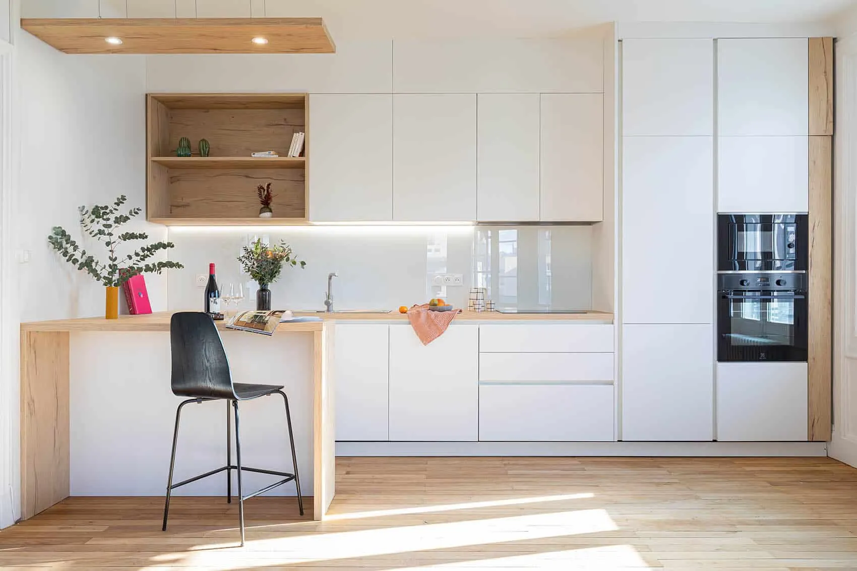 Cuisine sur mesure blanche et bois clair : retour bar avec tabouret, niches ouvertes et colonne de fours encastrés
