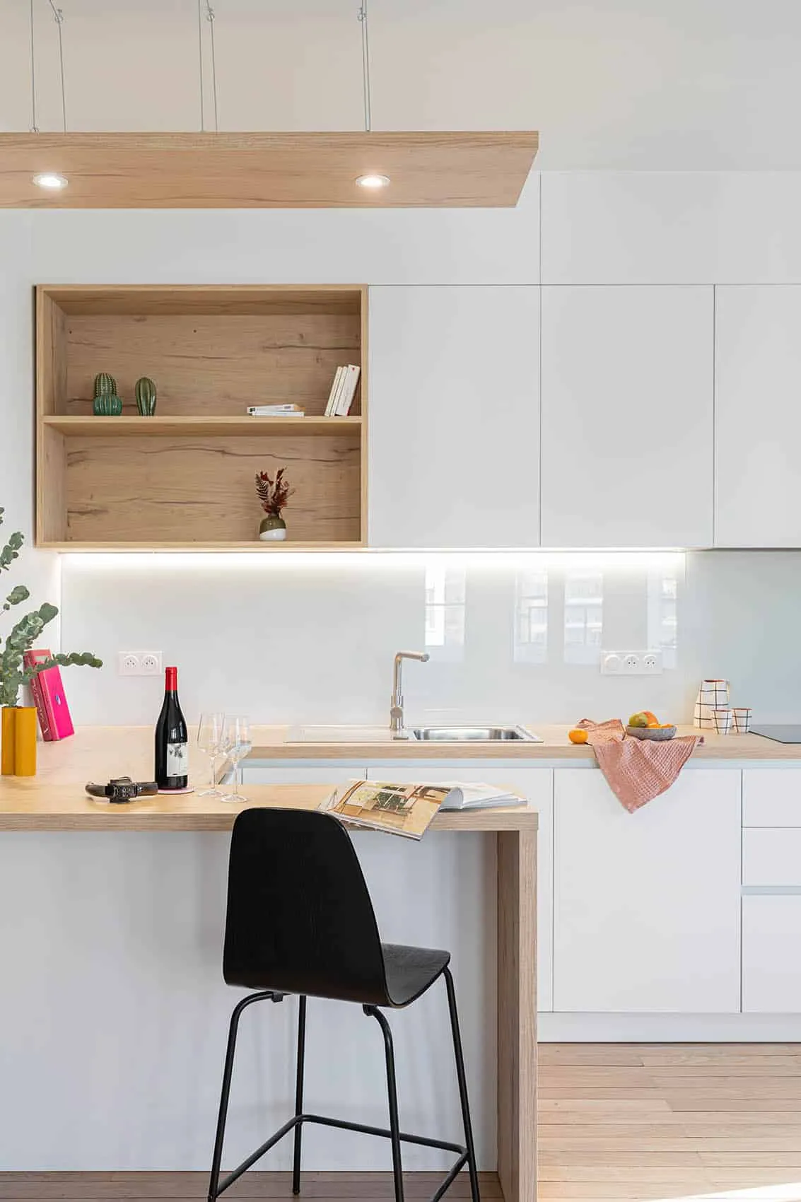 Plan snack en bois clair et crédence en verre blanc éclairée sous les meubles hauts de la cuisine