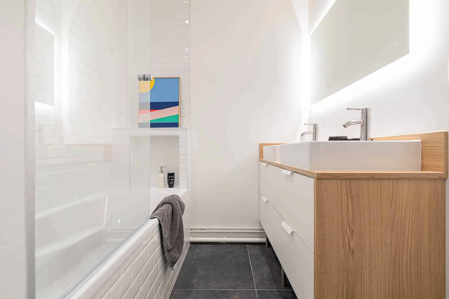Salle de bain blanche avec baignoire, carrelage métro, sol anthracite et long meuble double vasque en bois