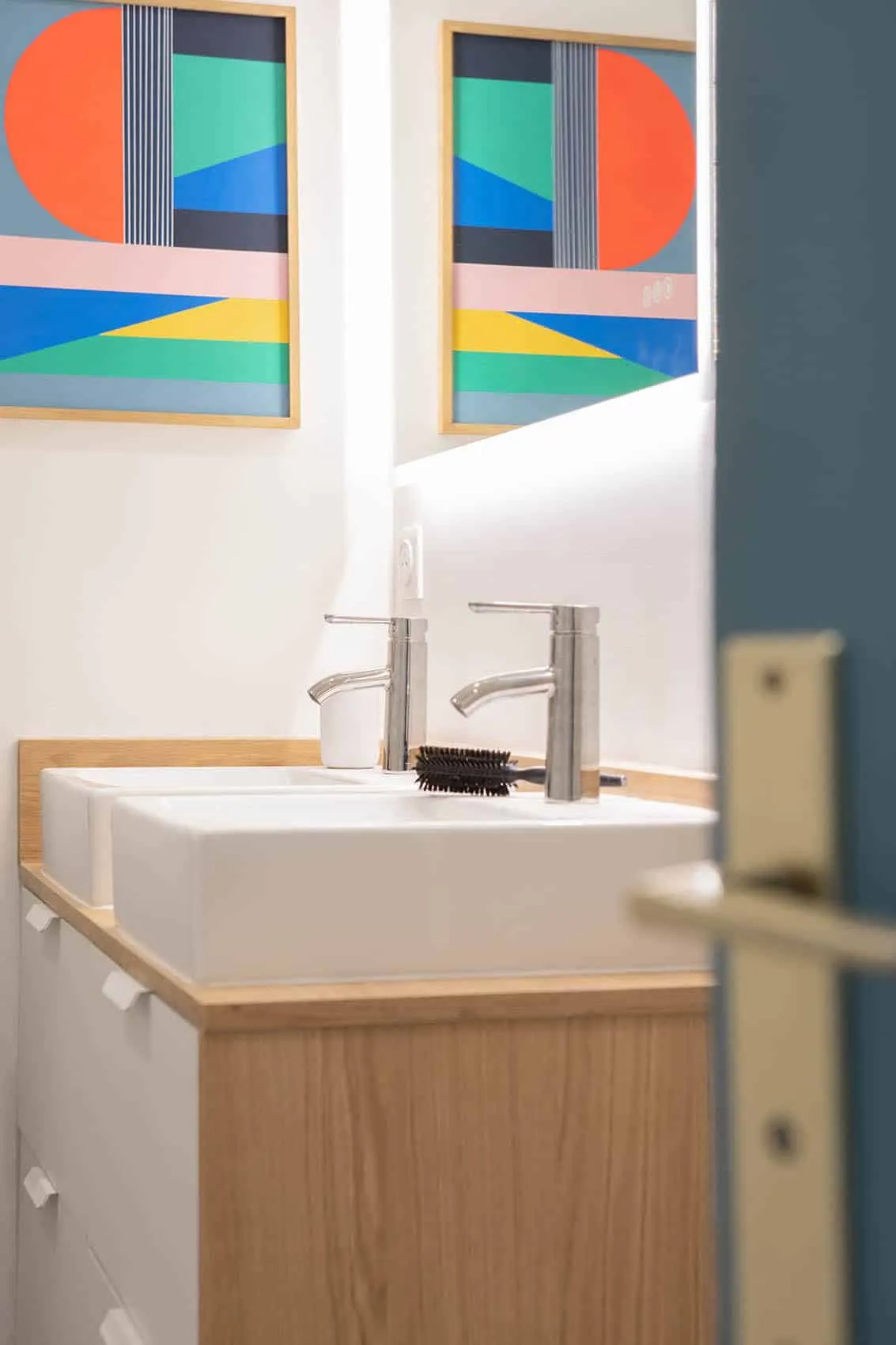 Double vasque blanche et mitigeurs inox sur plan en bois, porte bleue entrouverte de la salle de bain