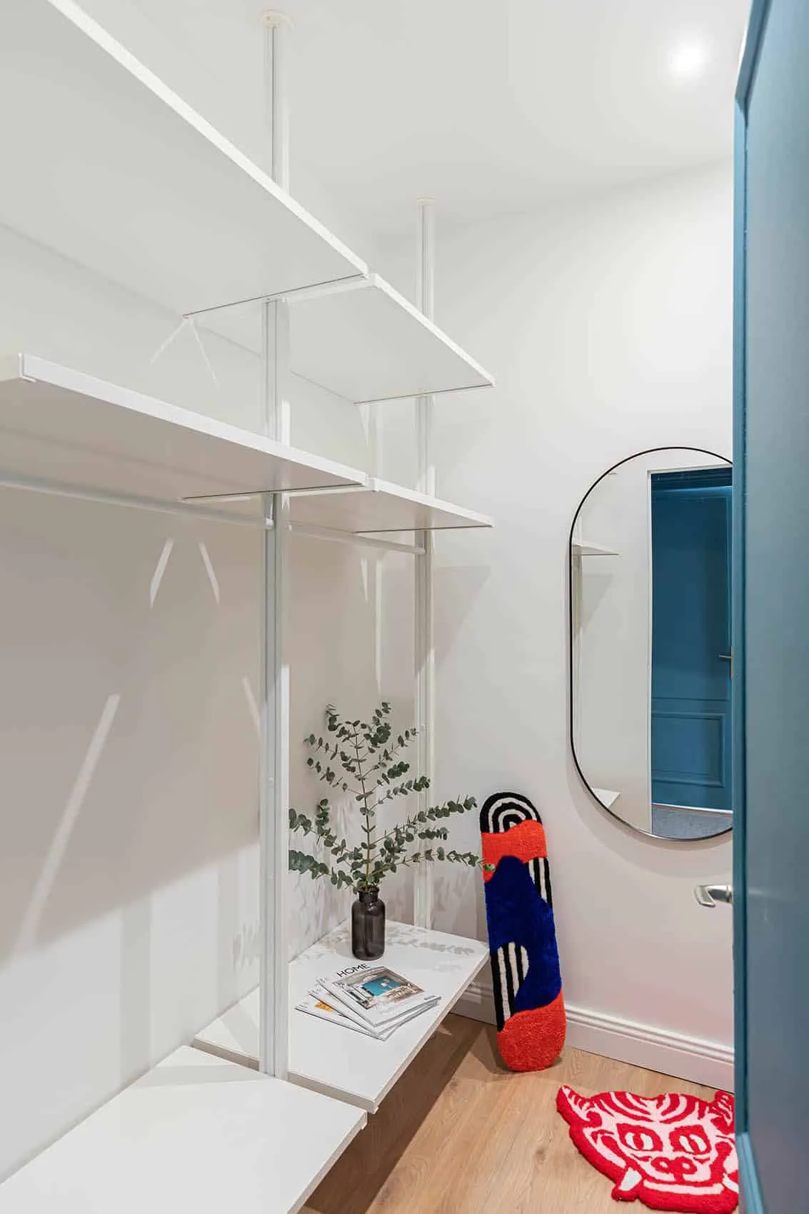 Vestiaire aux penderies et étagères blanches, miroir ovale et porte bleue, rangements sur mesure