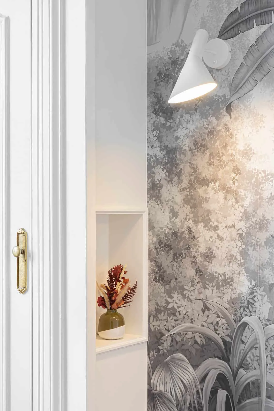 Papier peint à feuillage gris dans une niche, poignée de porte en laiton et bouquet séché