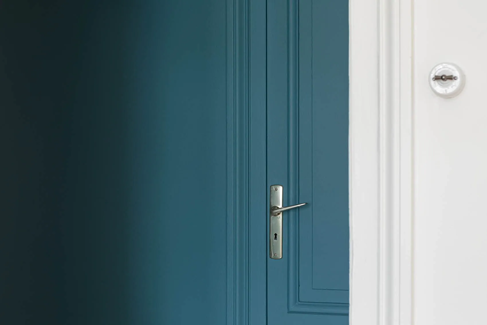 Porte moulurée peinte en bleu canard, poignée chromée et interrupteur rétro, entrée de l’appartement