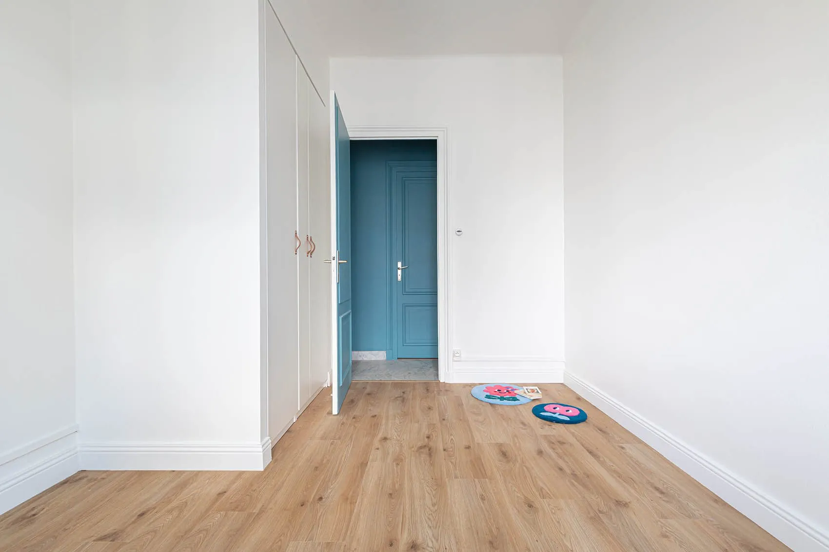 Chambre aux murs blancs et parquet clair, perspective sur une porte bleue, projet d’un architecte d’intérieur à Lyon
