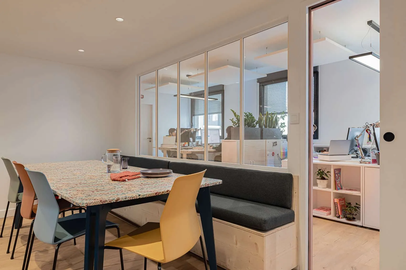 Salle de pause contemporaine avec banquette sur mesure et bureaux ouverts séparés par des verrières, réalisée par une agence d'architecture d'intérieur à Lyon.