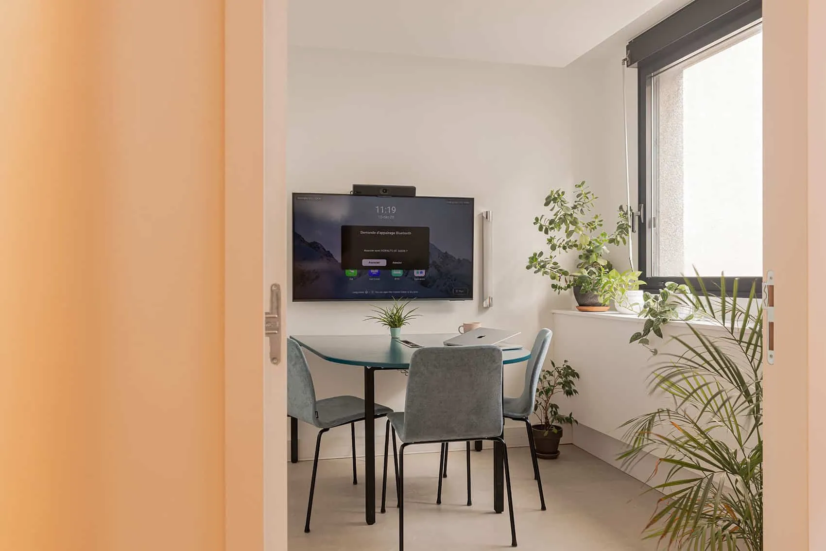 Petite salle de réunion avec table ronde, écran mural et plantes, aménagement d'espace professionnel
