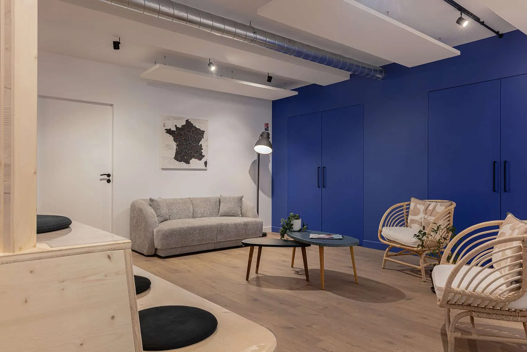 Espace de détente avec canapé gris, fauteuils en rotin et mur bleu Klein, aménagement de bureaux par Picture Design