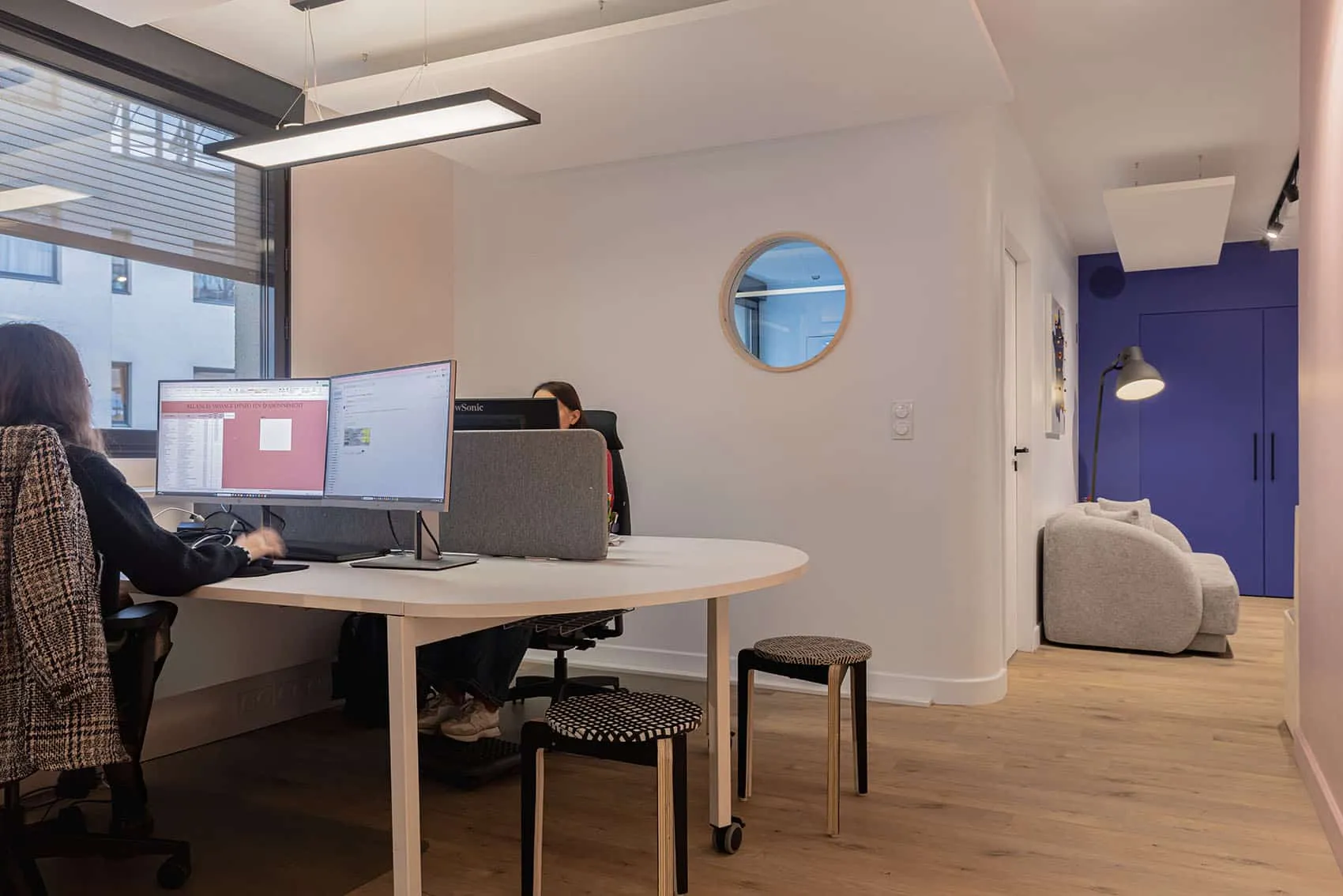 Open space avec bureau en bois arrondi, hublot et mur bleu Klein en fond, aménagement d'espaces de travail à Lyon