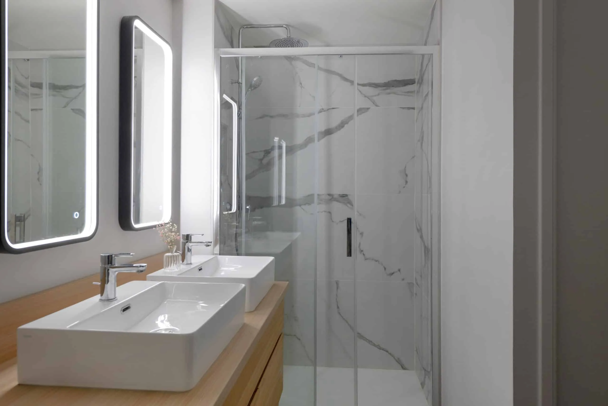 Double vasque blanche, miroirs lumineux et paroi de douche vitrée, salle de bains d’un appartement rénové à Lyon