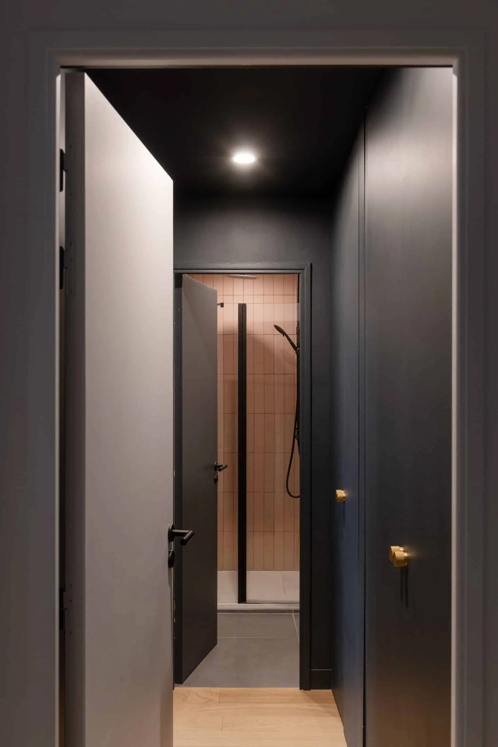 Couloir sombre menant à la salle d’eau au carrelage vieux rose et à la douche à robinetterie noire