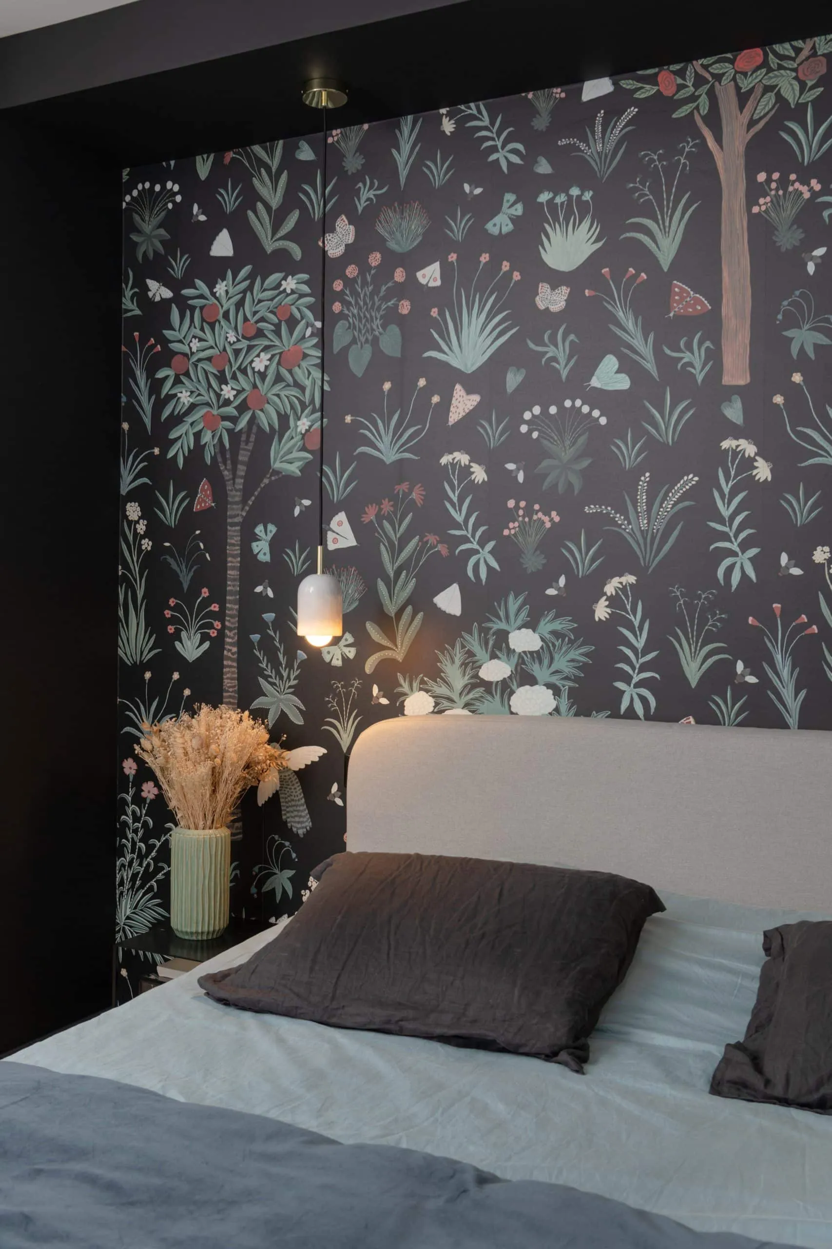Tête de lit arrondie claire et bouquet de fleurs séchées devant le papier peint botanique de la chambre