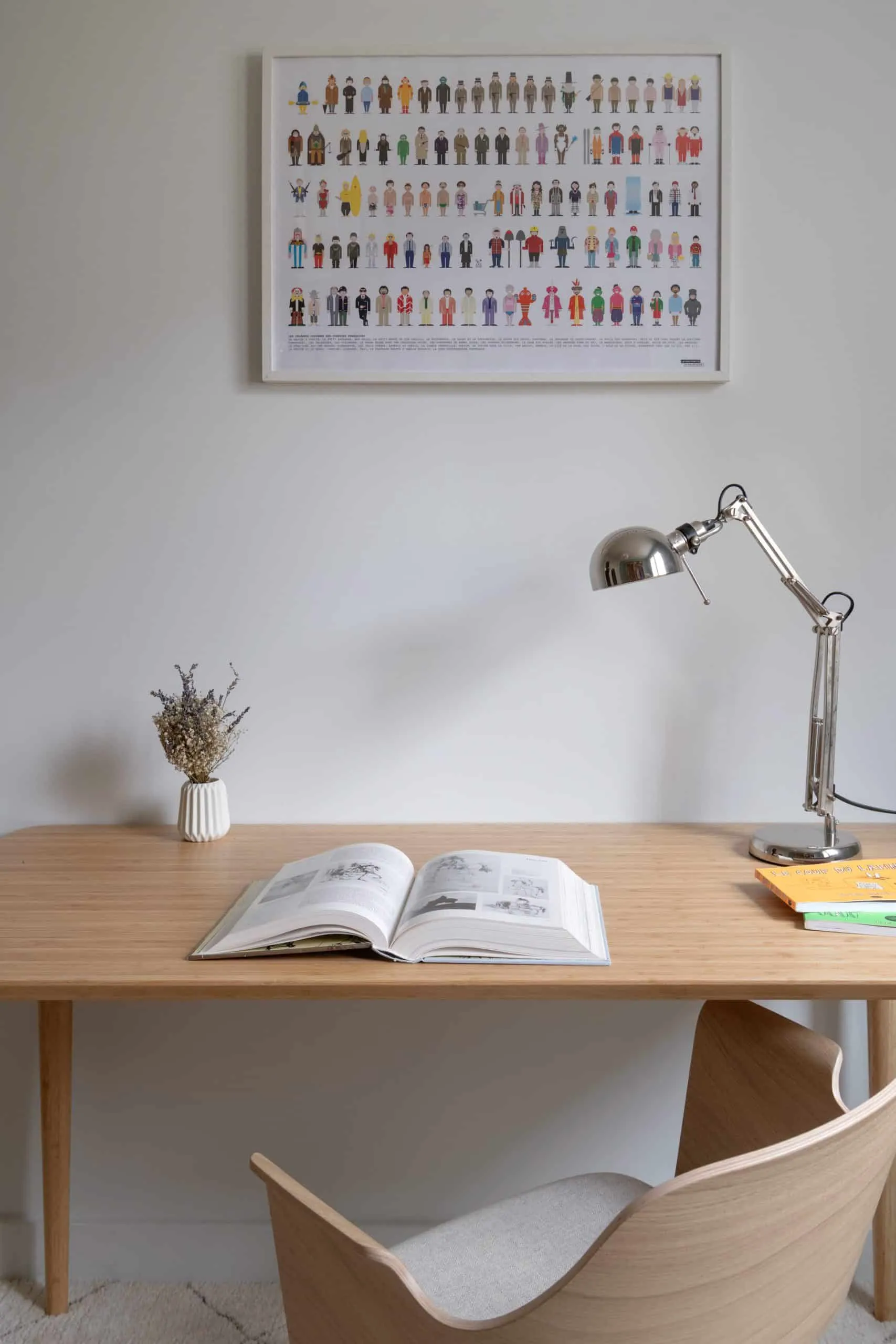 Détail du bureau en bois clair : livre ouvert, lampe d’architecte et petit bouquet de fleurs séchées