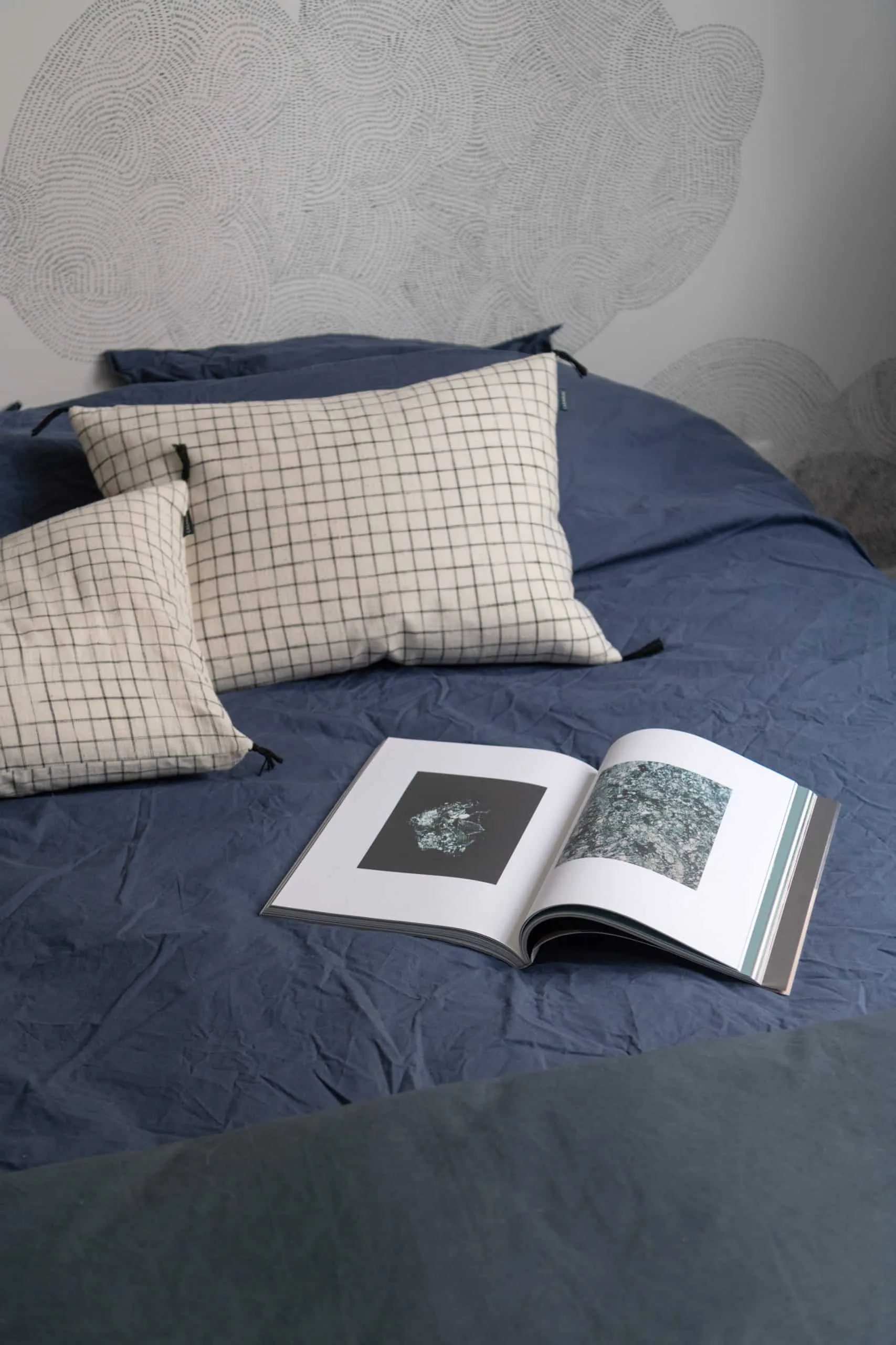 Linge de lit bleu marine, coussins à carreaux et livre ouvert dans une chambre de l’appartement Bugeaud