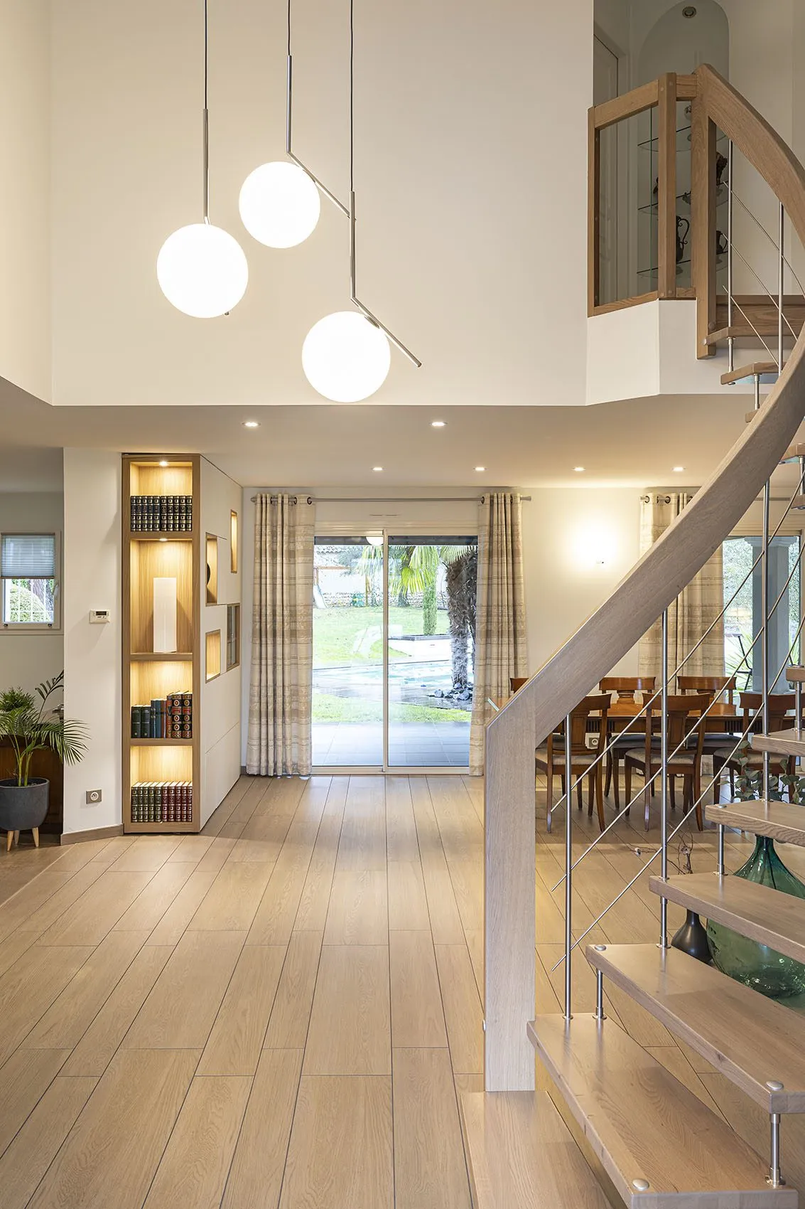 Pièce de vie ouverte sur le jardin, bibliothèque éclairée et salle à manger au pied de l’escalier contemporain