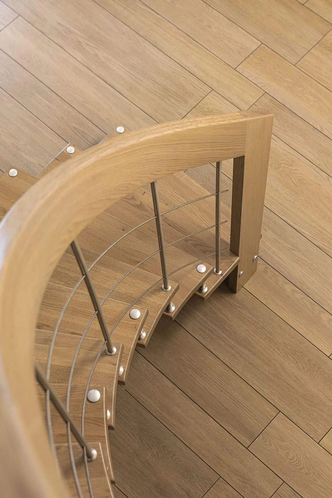 Vue plongeante sur la main courante courbe en bois et les marches de l’escalier, sol en carrelage effet bois