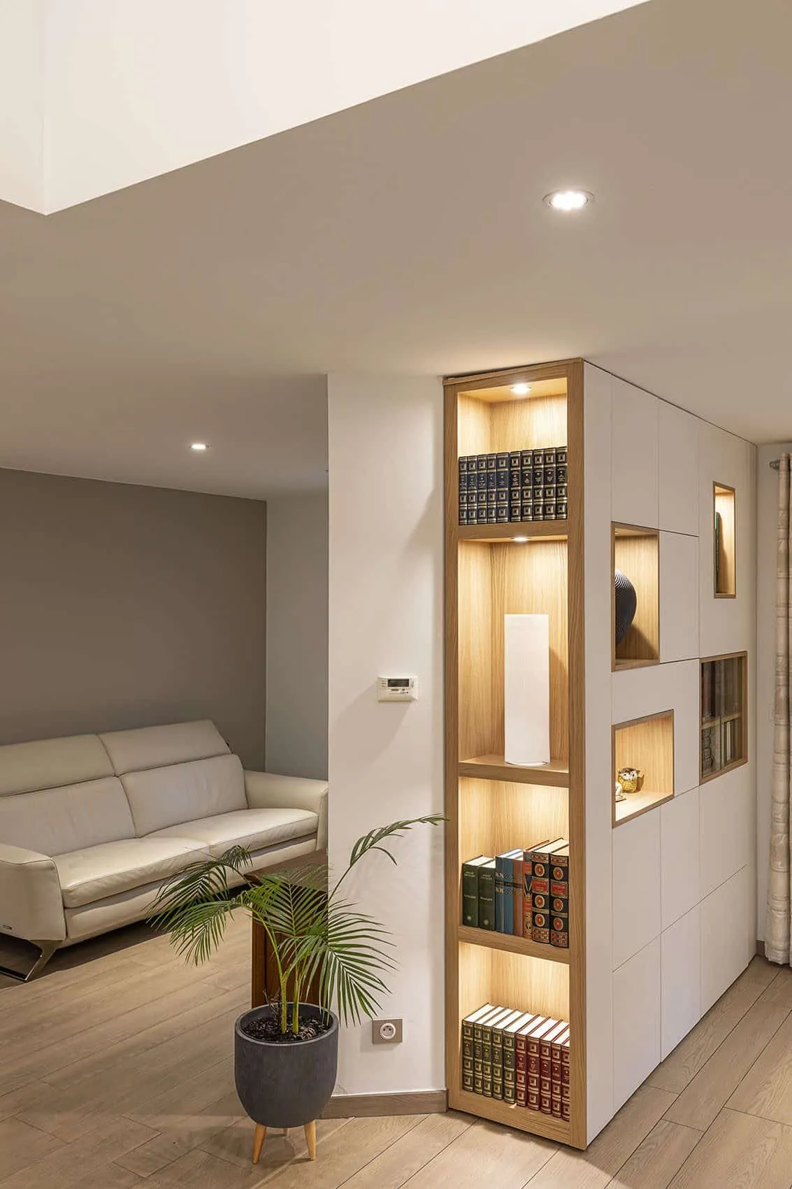 Bibliothèque sur mesure aux niches éclairées en bois clair à côté du canapé blanc de la pièce de vie