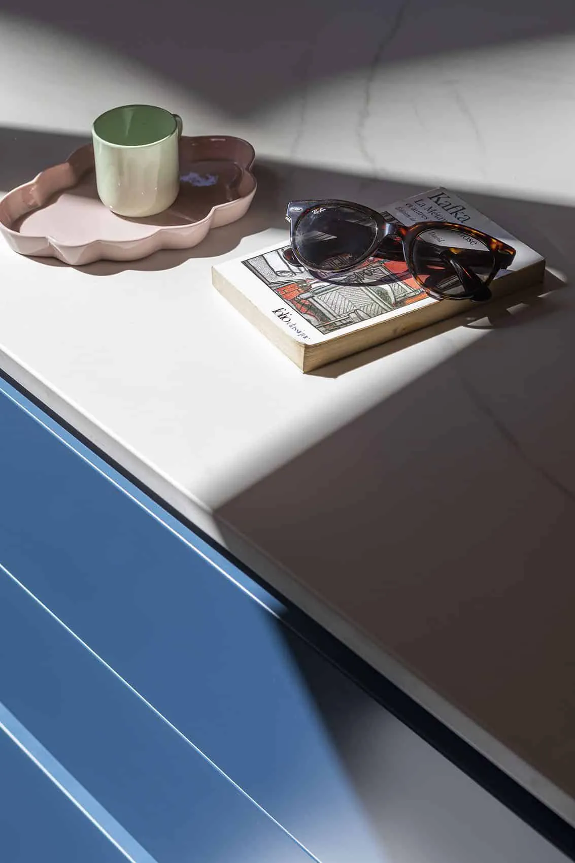 Plan de travail en Dekton blanc sur meubles bleus de la cuisine du canut Bon Pasteur, magazine et lunettes posés en angle