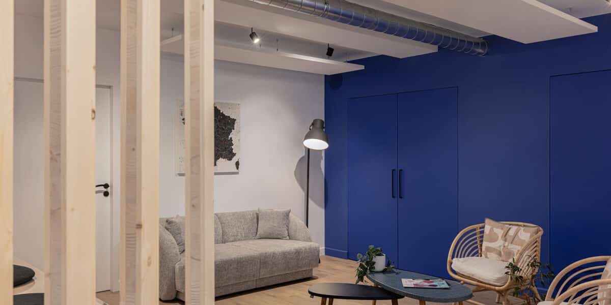 Espace de détente aménagé dans des bureaux à Lyon : cloison bois, canapé gris, fauteuils en rotin et mur bleu Klein, réalisé par Picture Design
