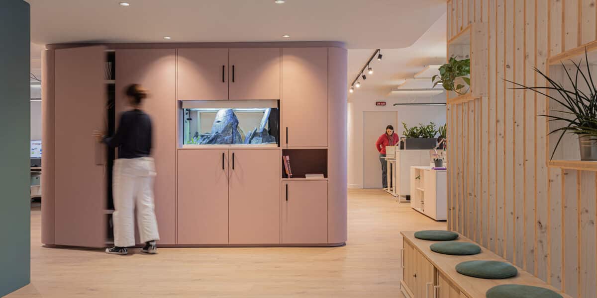 Volume de rangement arrondi rose poudré avec aquarium intégré, cloison claire-voie en pin et espaces de travail ouverts – bureaux Cap'Com à Lyon par Picture Design